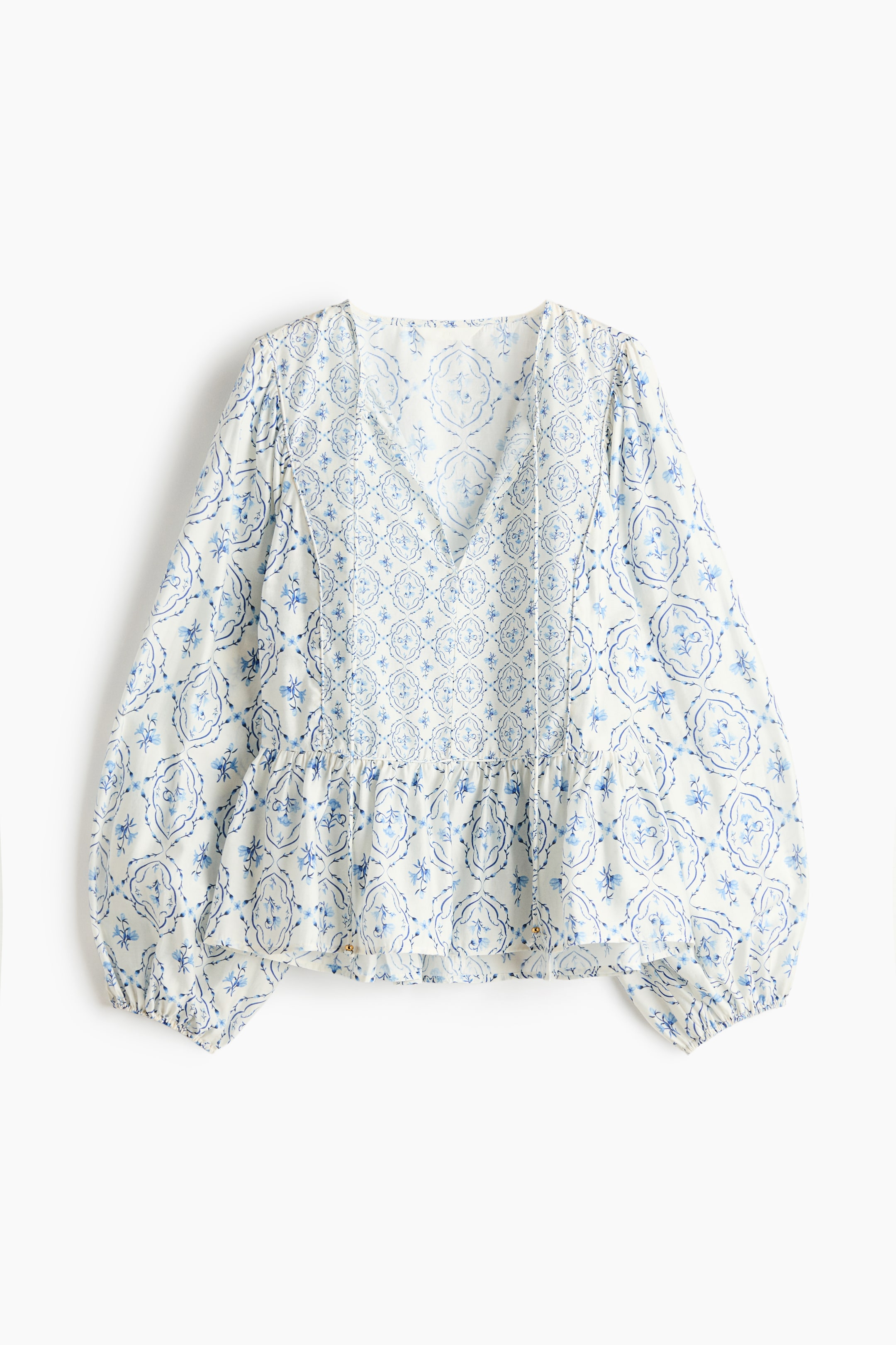 Ver imagen más grande: La PARTE DELANTERA de una blusa blanca con un patrón similar a azulejos azules presenta un escote redondo con una abertura en forma de V y cintas finas de espagueti rematadas con cuentas, mangas largas abullonadas con puños elásticos estrechos, un péplum acampanado y pliegues verticales en el frente del cuerpo.