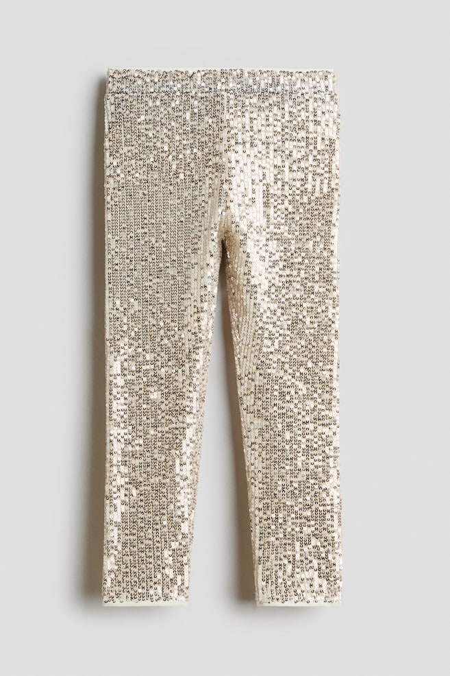 Eine goldfarbene Leggings mit Pailletten wird von vorne gezeigt. Sie verfÃ¼gt Ã¼ber einen elastischen Bund und eine schmale, zum Bein hin schmal zulaufende Silhouette. Dicht angeordnete Pailletten bedecken die gesamte OberflÃ¤che des KleidungsstÃ¼cks und sorgen fÃ¼r ein schimmerndes, strukturiertes Finish. - 1