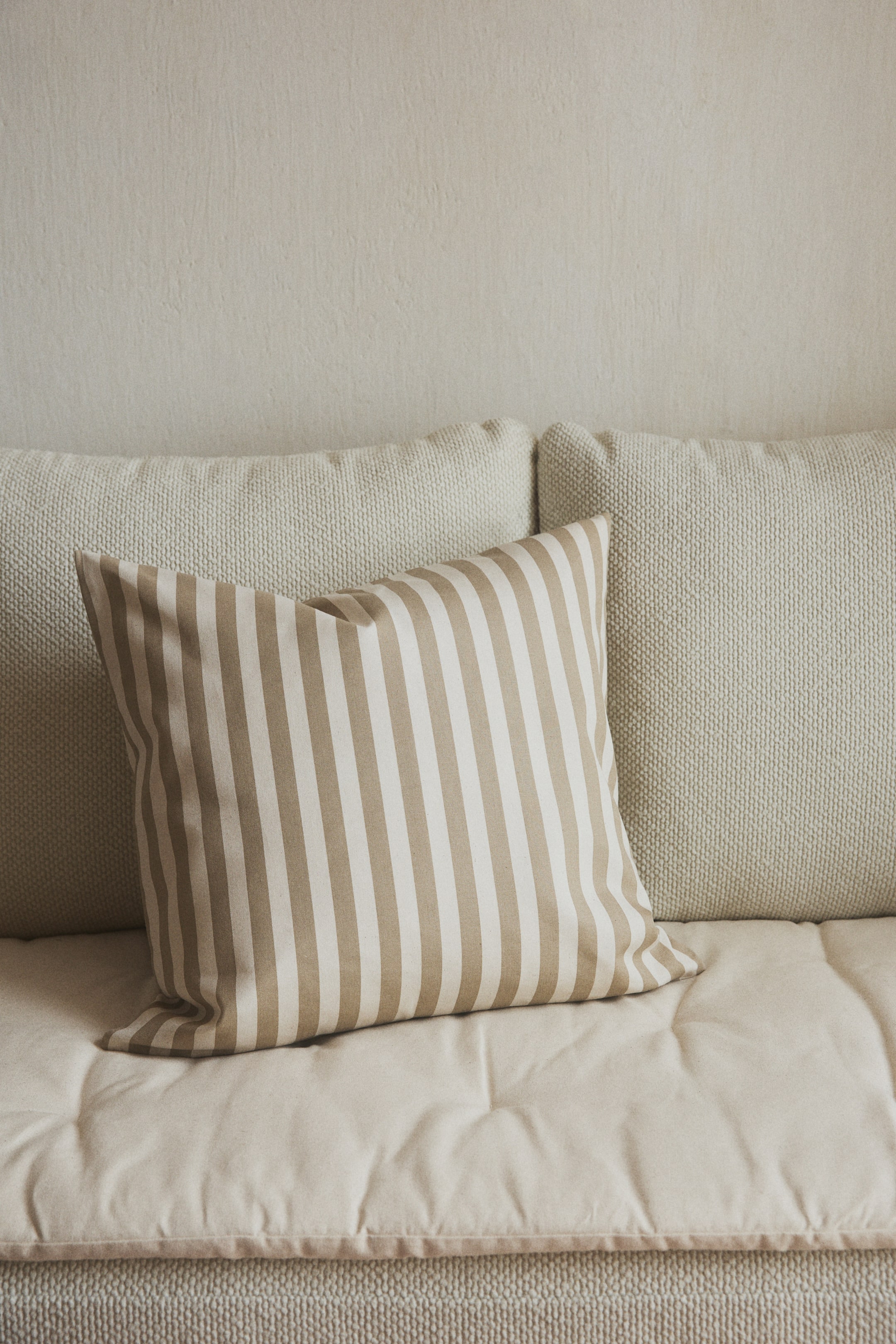 View larger image: "A water-repellent cotton canvas cushion cover is appearing plump, its front displaying alternating vertical stripes of light beige and off-white."