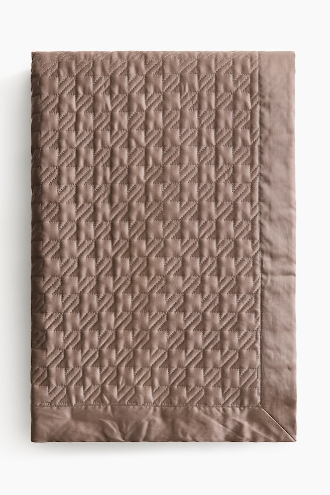 A brown quilted blanket showcases a repeating stepped geometric stitch pattern across its surface. It features a plain, smooth border along its edges. - 1