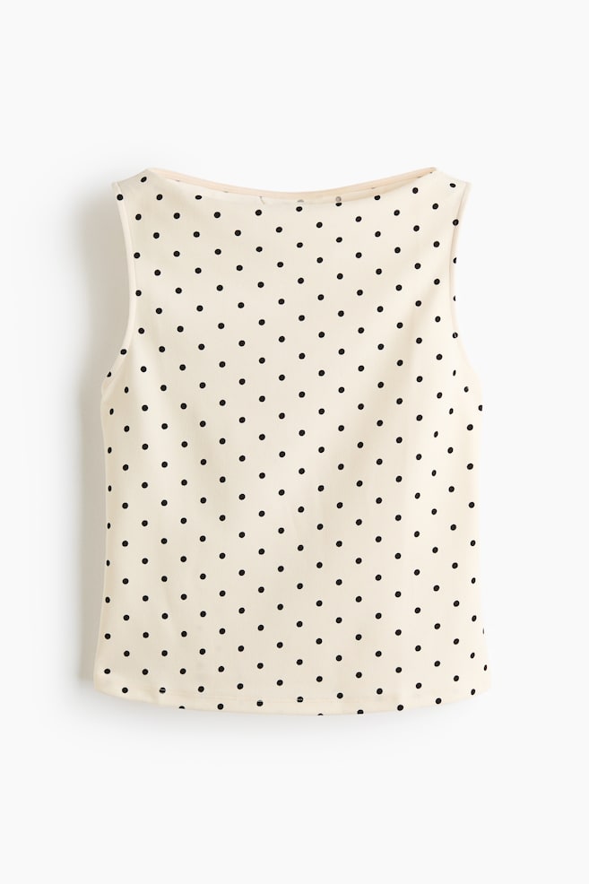 A sleeveless top featuring cream fabric patterned with small, evenly spaced black polka dots. It presents a wide, shallow boat neckline and finished armholes. - 1