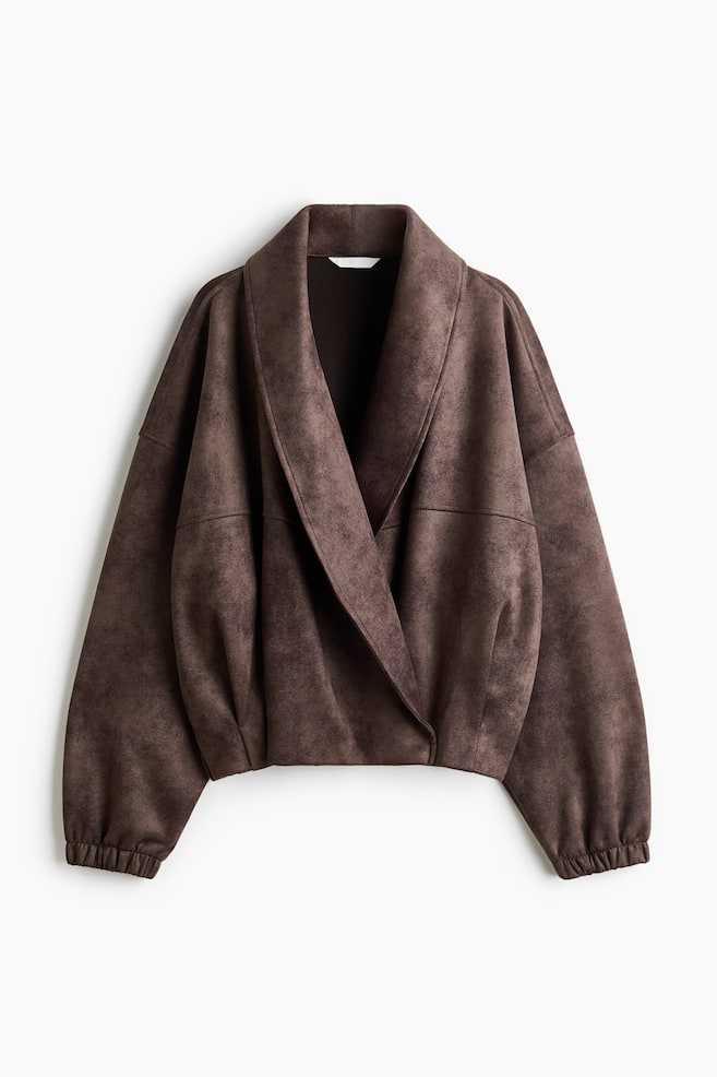 Una giacca in finta pelle scamosciata marrone Ã¨ presentata in una vista frontale, mettendo in risalto una silhouette rilassata con un ampio collo a scialle drappeggiato e un davanti incrociato sovrapposto. Il design presenta spalle scese e maniche lunghe e ampie che terminano con polsini elasticizzati arricciati. - 1