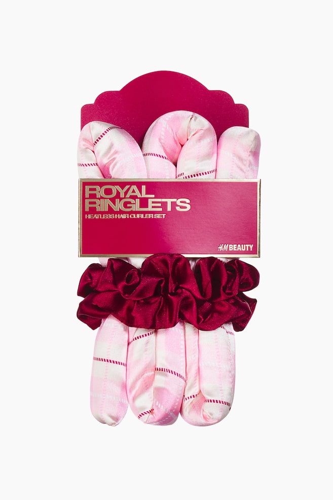 Ett vÃ¤rmefritt hÃ¥rcurlar-set visas i frontvy och framhÃ¤ver en rosa- och vitrutigt satinlockstav insvept med en mÃ¶rkrÃ¶d satin-scrunchie. Setet ligger pÃ¥ en magenta kartongbakgrund med ett matchande pappersband som visar produktnamnet "ROYAL RINGLETS" i guldfÃ¤rgade bokstÃ¤ver. - 1