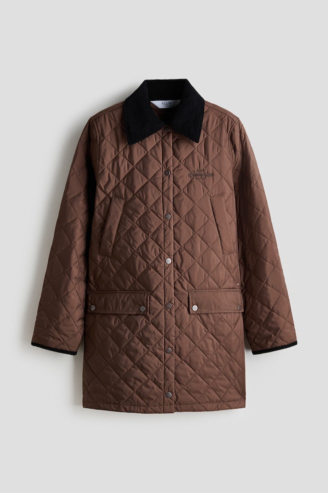 The front of a brown diamond-quilted stable jacket displays a black corduroy collar and an embroidered "ALLIN Equestrian" motif on the chest. It features a front placket with dark press-studs, diagonal hand-warming pockets, flap front pockets with press-stud fastening and narrow ribbed cuffs. - 1
