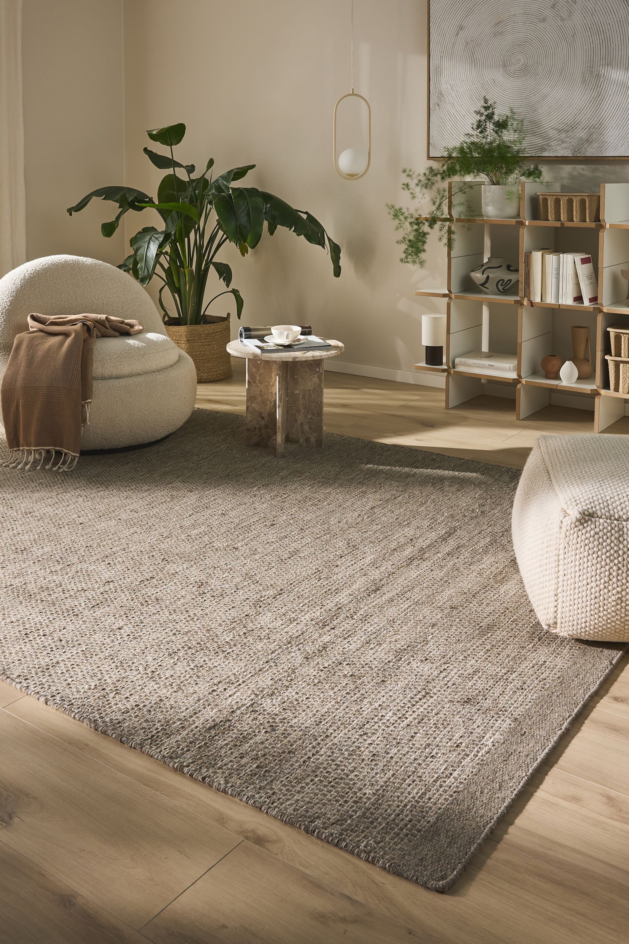 Agrandir l'image: Un tapis rectangulaire s'étend sur le sol, affichant une texture tissée de fibres naturelles grossières et mouchetées dans des nuances de brun clair et de beige. Ses bords visibles sont soigneusement finis.