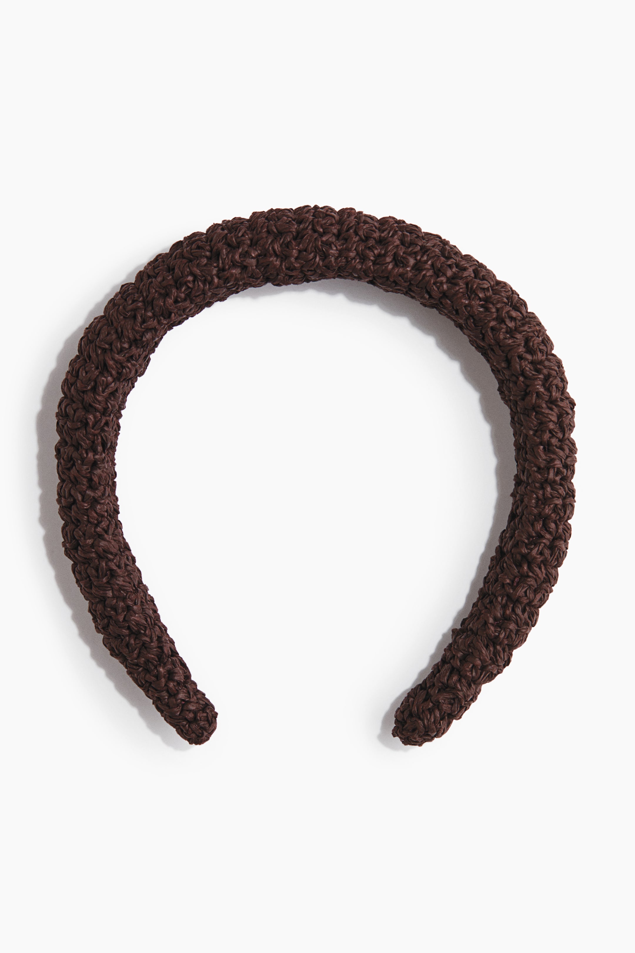 Grotere afbeelding bekijken: Een bruine, U-vormige haarband toont een dik, gewatteerd ontwerp met een geweven, gestructureerd oppervlak.