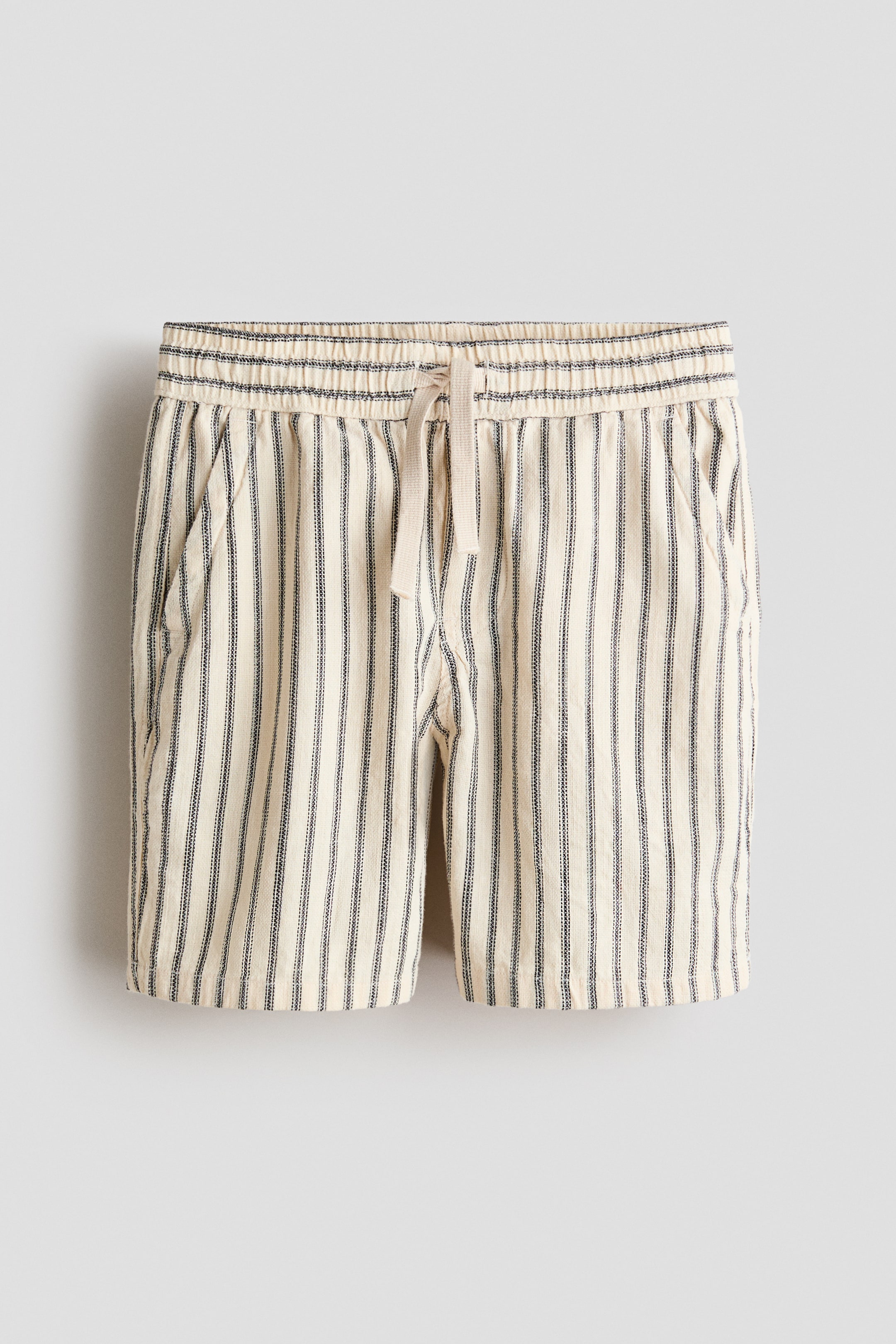 View larger image: The loose-fit shorts showcase a textured, off-white cotton weave with slim black vertical stripes. They feature an elasticated drawstring waist complete with a tied beige drawstring, a faux fly, and diagonal front pockets.