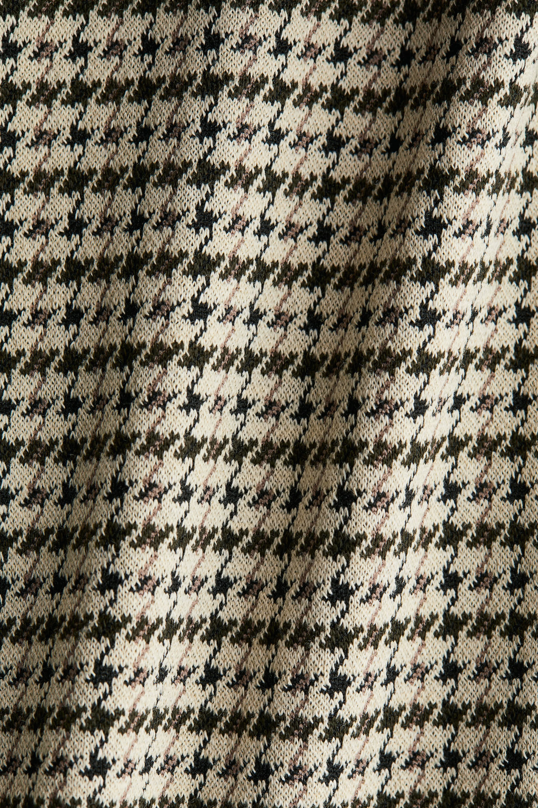 Xem ảnh lớn hơn: Một loại vải đang có họa tiết houndstooth cổ điển với màu kem, xanh đậm và đen, cùng với các đường chéo màu nâu đỏ nhạt. Nó hiển thị kết cấu đan và các nếp gấp nhẹ nhàng.