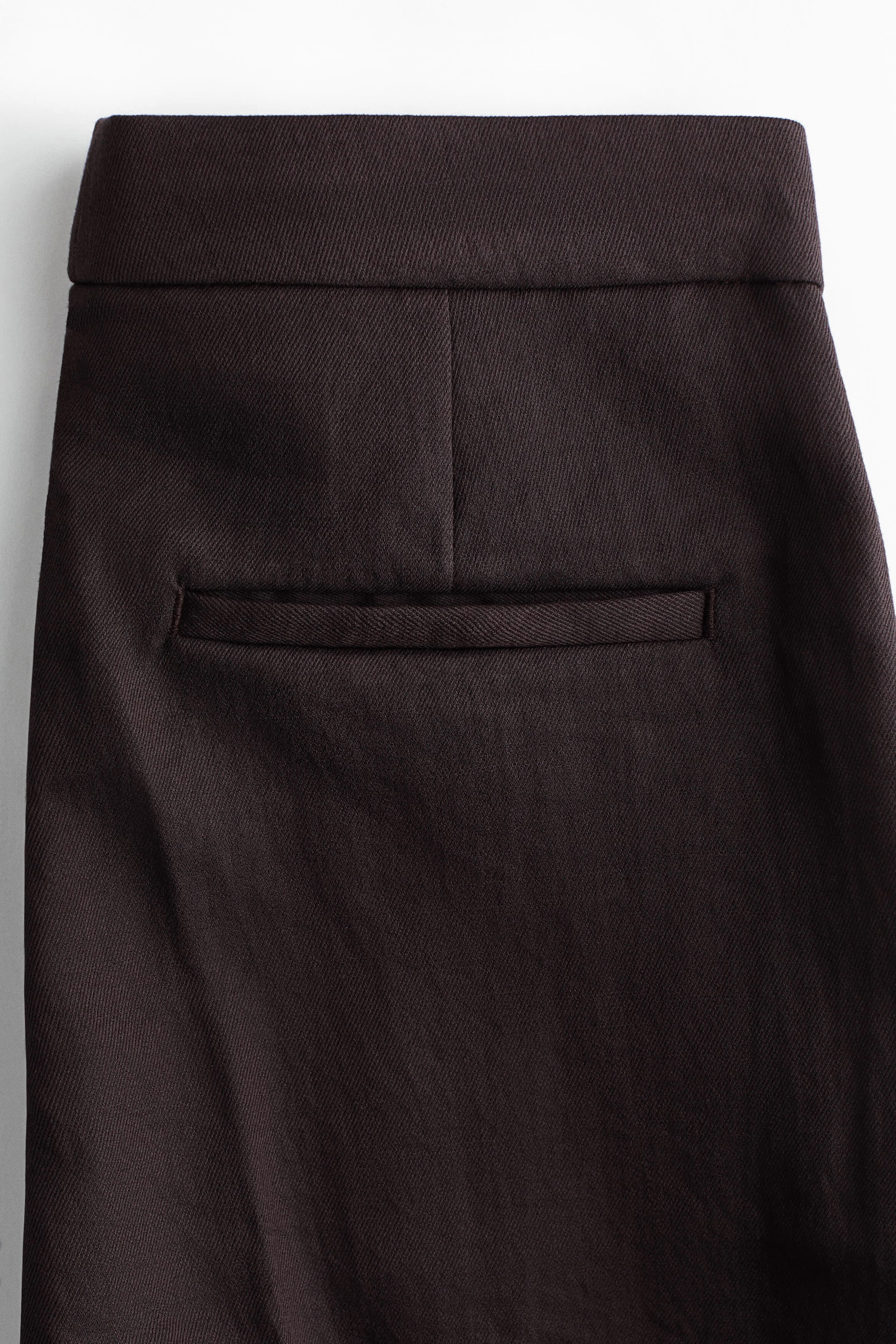 Voir une image plus grande: Les pantalons sur mesure présentent une taille haute et étendue ainsi qu'une poche arrière passepoilée unique, le tout dans un tissu tissé brun foncé.