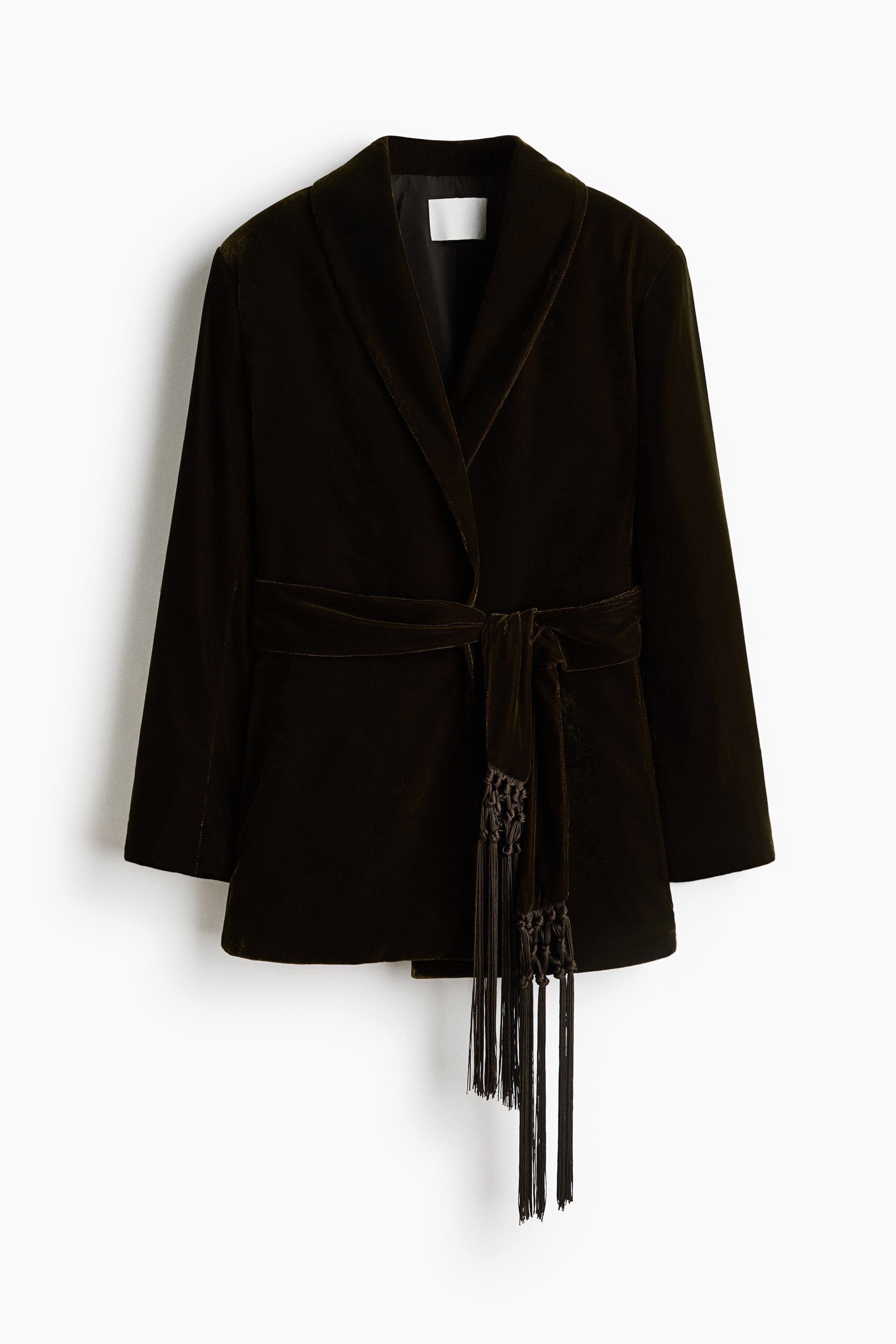 View larger image: A dark brown velvet wrap jacket is shown from the front, featuring a shawl collar, long sleeves, and a matching velvet belt tied at the waist. The belt showcases long knotted fringe tassels draping down past the hem.