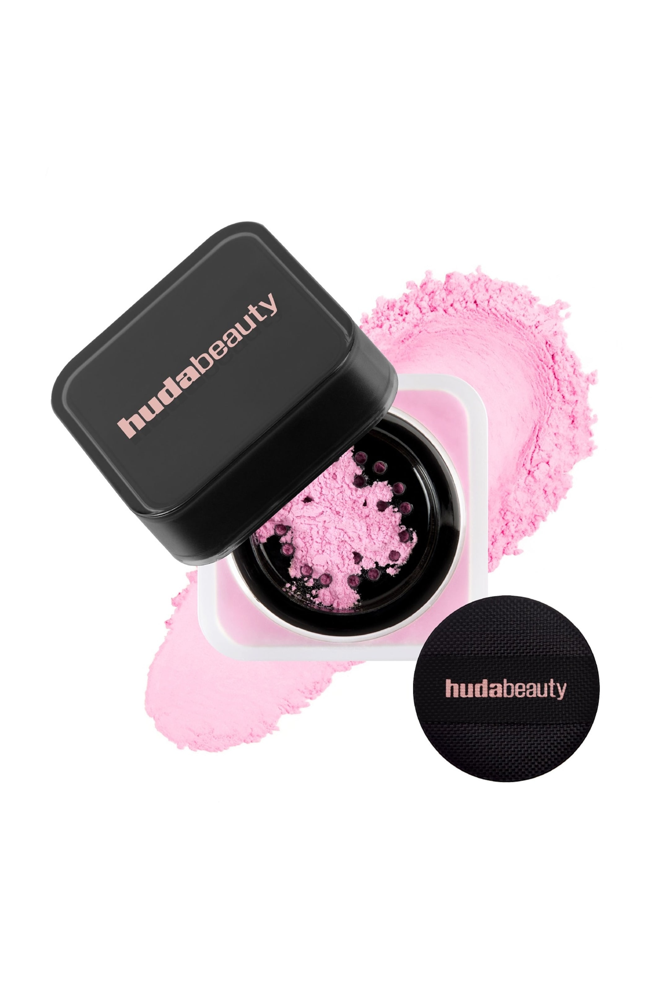 Visa större bild: En Huda Beauty löspuderbehållare är vinklad öppen, med ett svart fyrkantigt lock med varumärkets logotyp och en synlig sikt med ljusrosa puder inuti. Löspuder i rosa färg spills runt behållaren, och en svart cirkulär puff med varumärkets logotyp ligger i närheten.