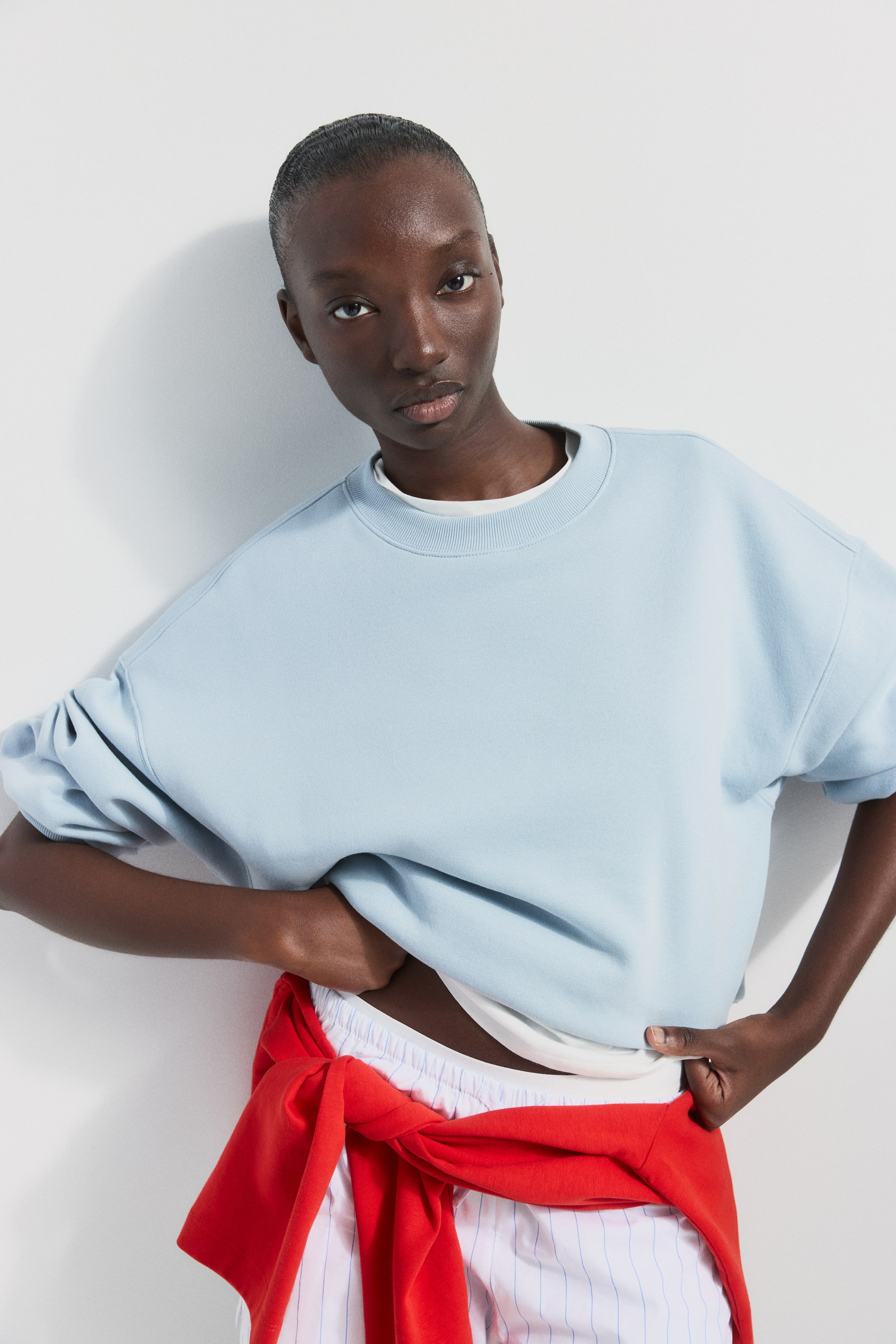 View larger image: The light blue sweatshirt showcases a ribbed crew neck and dropped shoulders. Its wide sleeves are pushed up, and the relaxed hem is visibly layered over a white t-shirt.