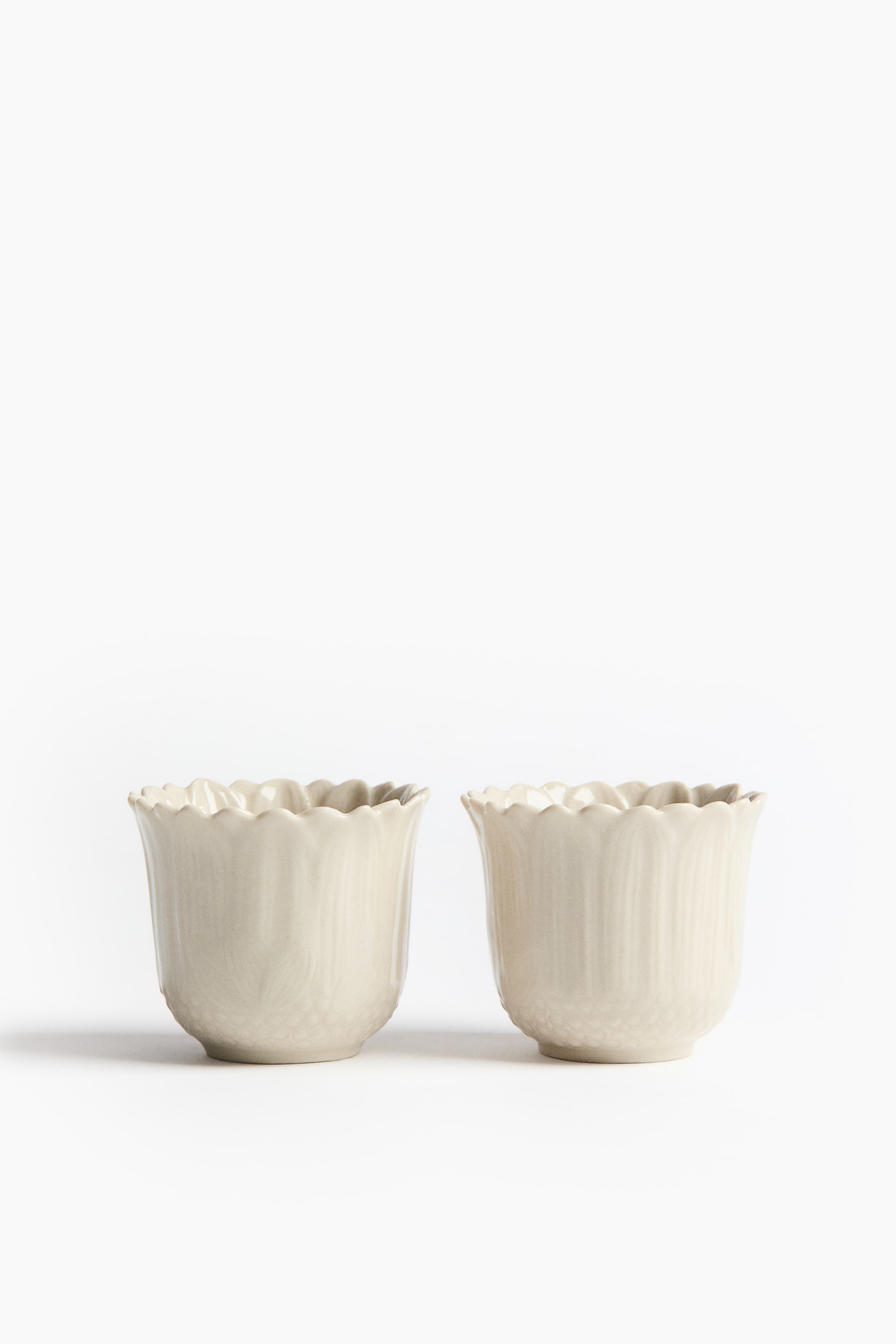 View larger image: Two cream-colored ceramic cups are standing side-by-side, facing front. Each cup features a scalloped rim and vertical fluting along its body.