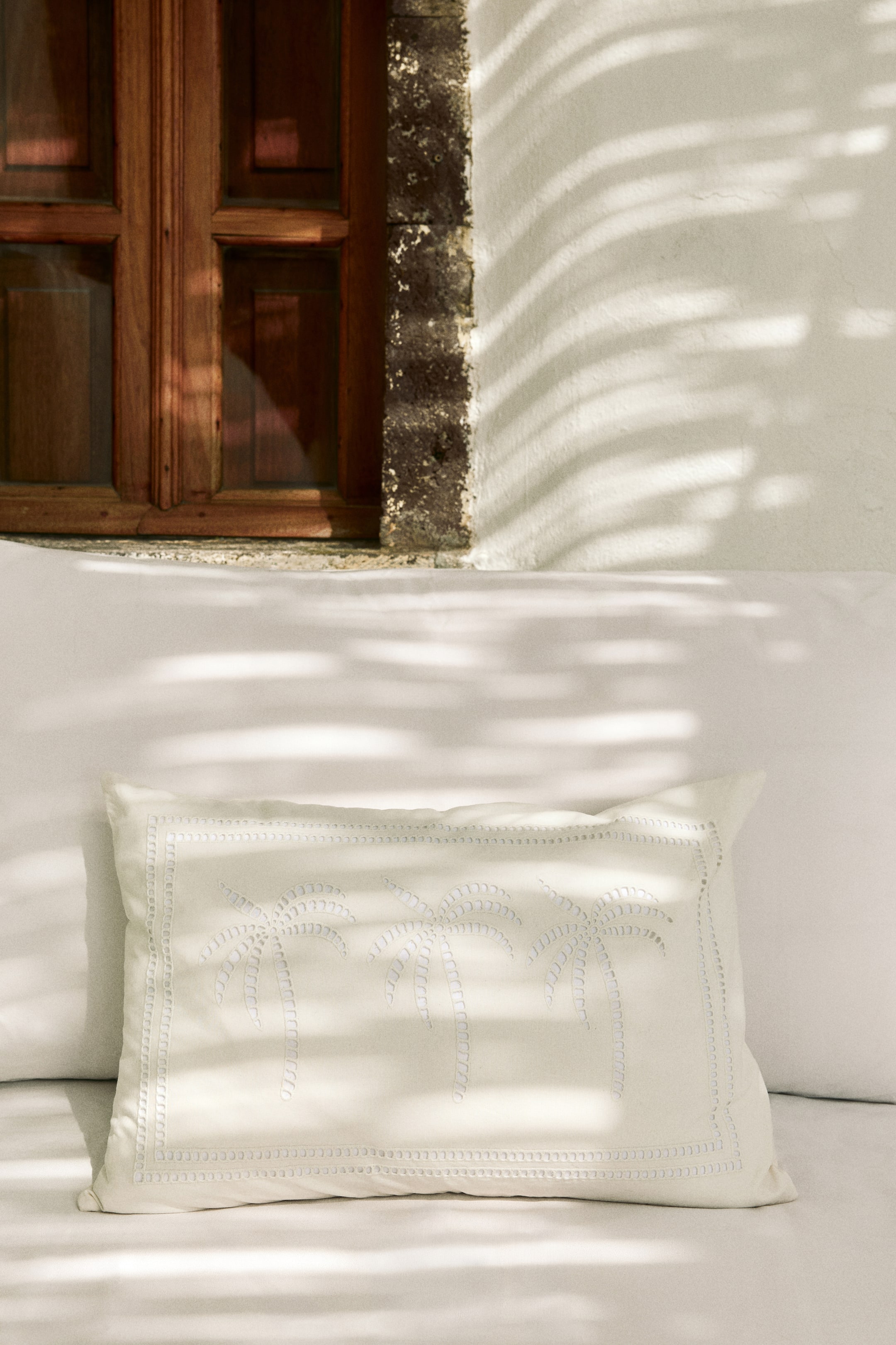 View larger image: A rectangular cream cushion lies flat, showcasing three light-coloured palm trees intricately embroidered on its front. A decorative stitched border frames the cushion's edges.