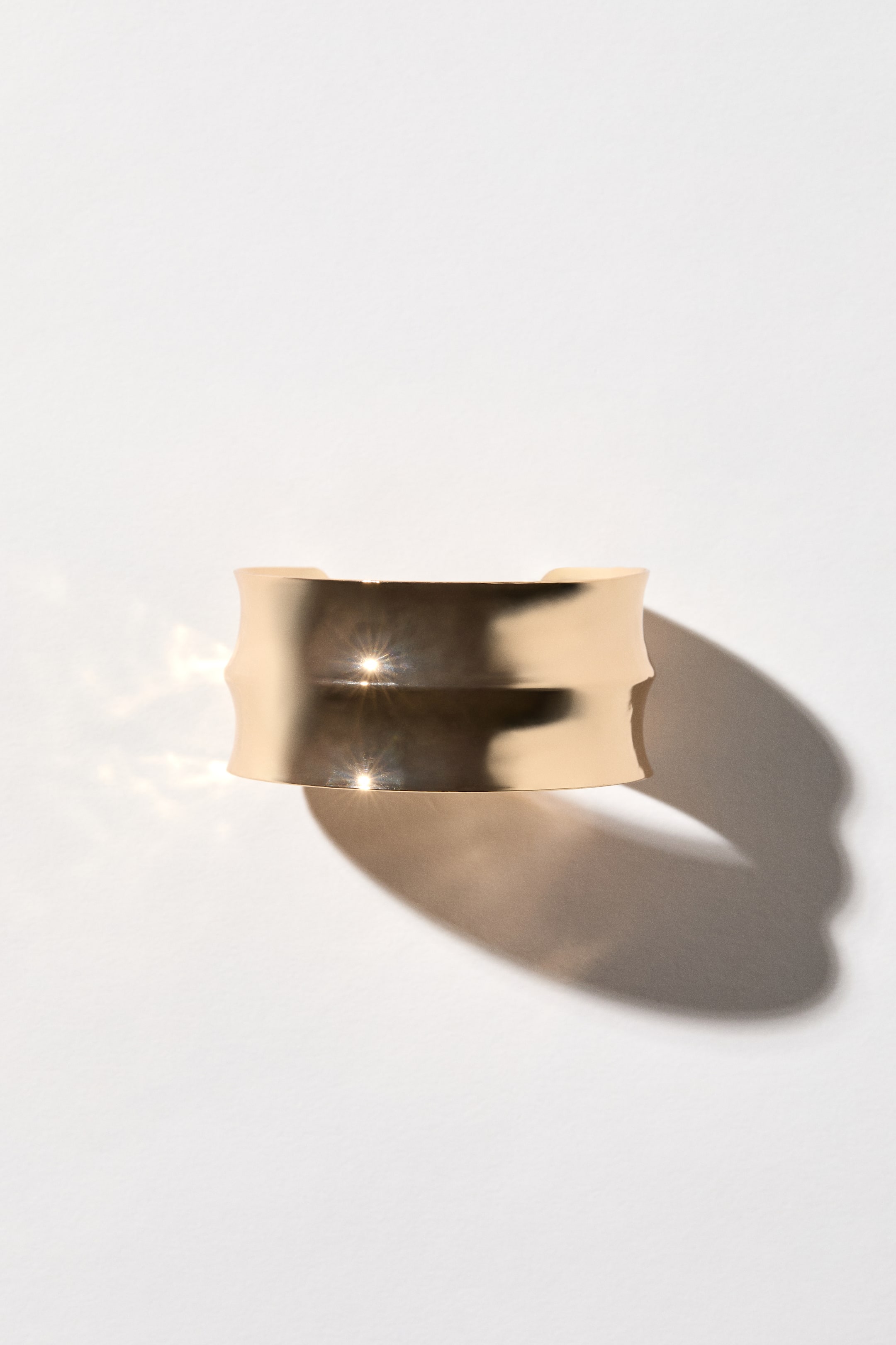 Ver imagen más grande: El brazalete de puño ancho presenta una superficie de metal brillante con un diseño acanalado que crea una onda central a lo largo de su parte frontal. Se muestra desde un ángulo frontal, exhibiendo su estructura amplia y abierta.