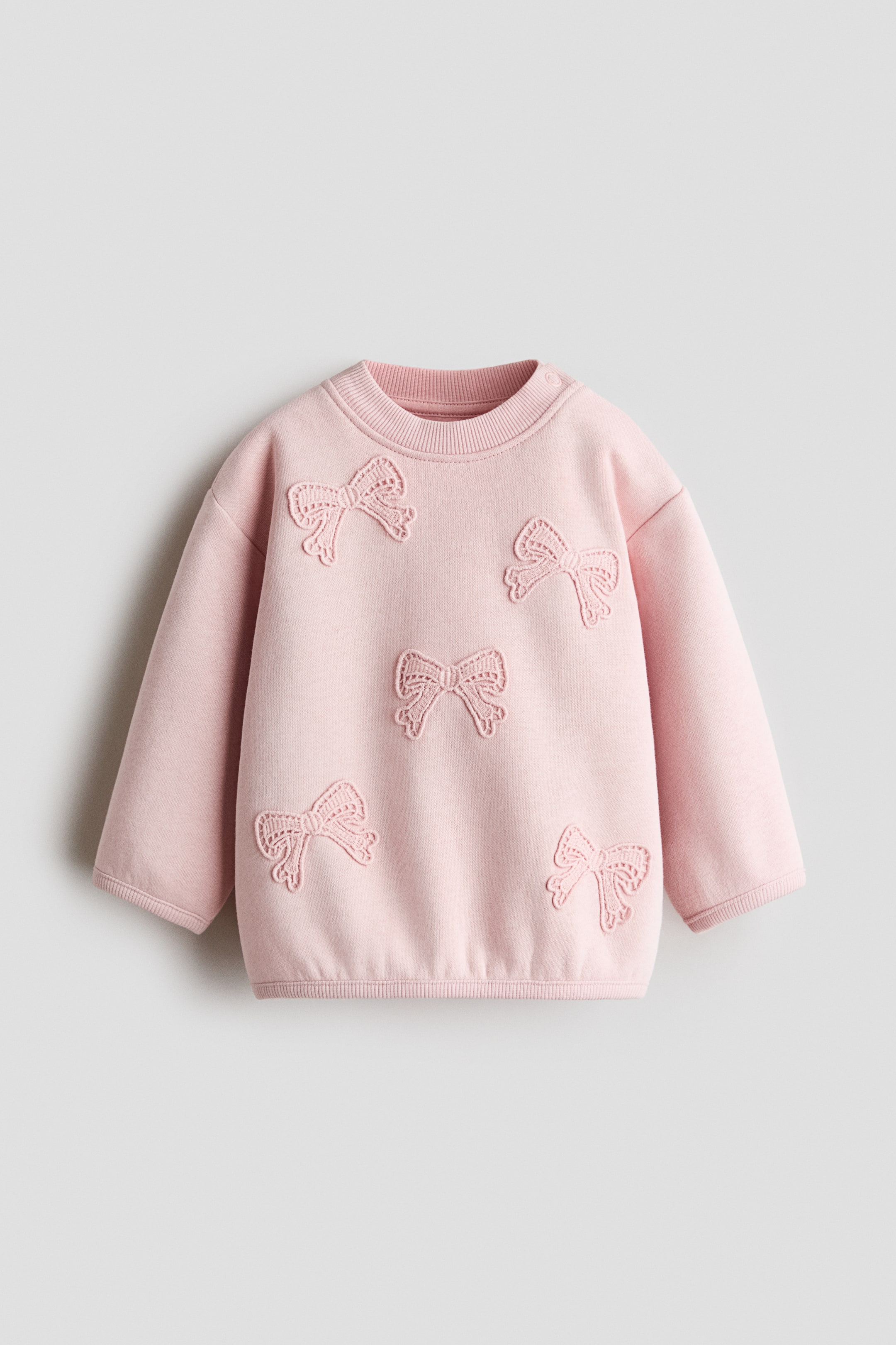 View larger image: The pink Design Detail Sweater is facing front, featuring five embroidered bow appliqués scattered across the body. It is displaying long sleeves with ribbed cuffs, a ribbed crew neck, and a ribbed hem.
