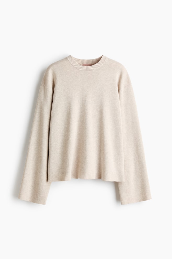 Un jersey de punto fino de color beige claro y de corte oversize cuelga de frente, mostrando un cuello redondo acanalado, hombros caÃdos y mangas largas y anchas. - 1