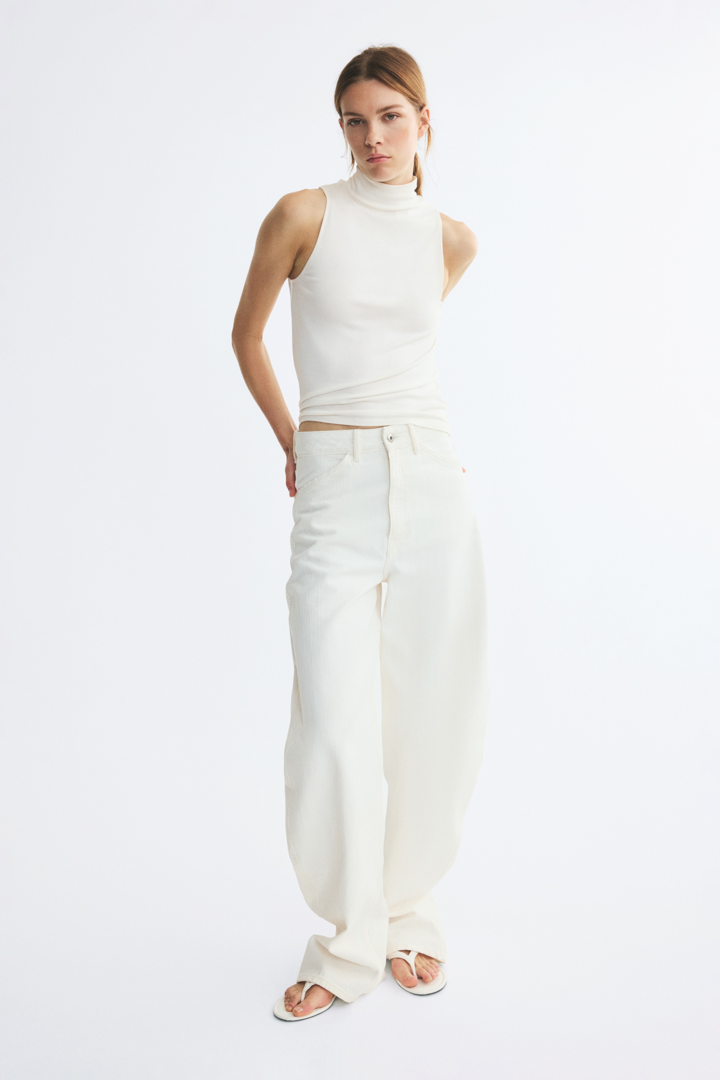 A cream sleeveless top is featuring a mock neck collar and clean-cut armholes, laying flat from a front-facing perspective.