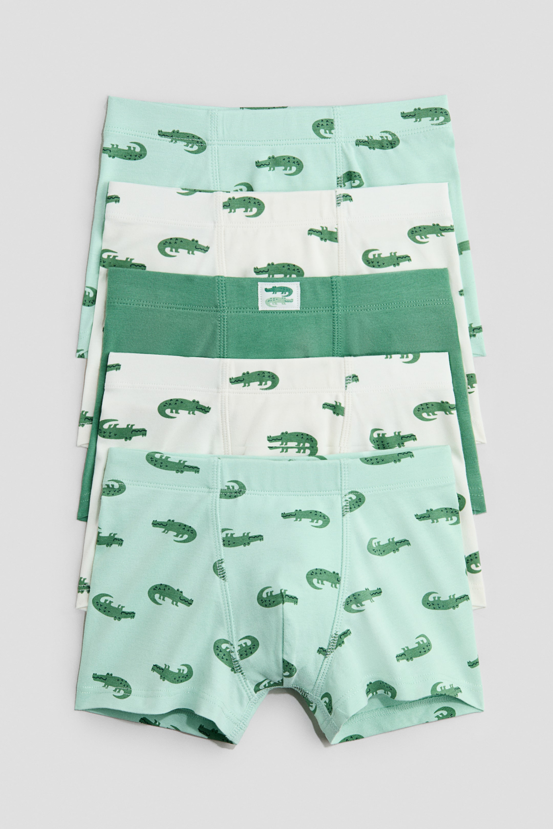 View larger image: Trunks crafted from cotton jersey, featuring short legs and an elasticated waist, are neatly arranged, showcasing their front. Three pairs come in a light green hue adorned with an allover green alligator print, one pair is white with a similar allover green alligator print, and another pair is a solid dark green, highlighted by a small alligator logo on the waistband.