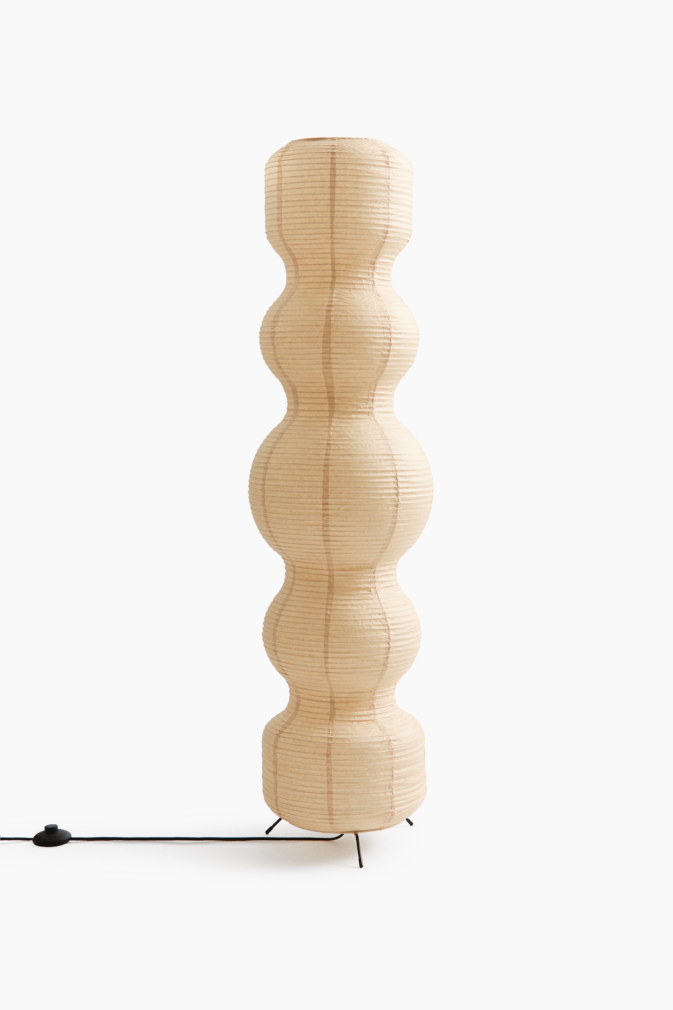 A floor lamp featuring a tall, sculptural off-white rice paper lampshade with a ribbed texture stands upright, showcasing an undulating silhouette made of five stacked, bulbous segments.