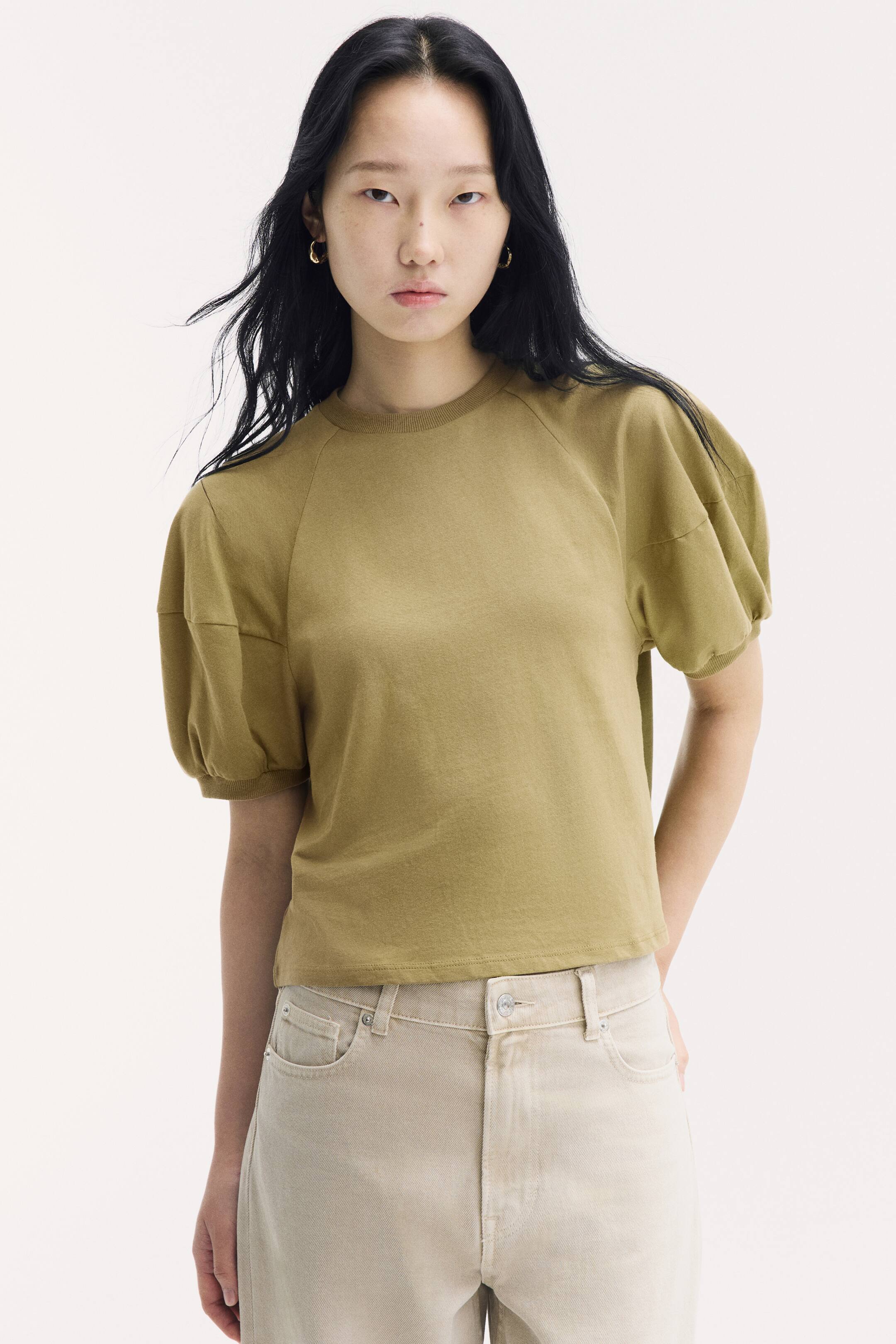 View larger image: An olive-green cotton jersey top featuring a round, rib-trimmed neckline and short, puffed raglan sleeves with ribbed cuffs is being worn by the model. The top is styled with light beige jeans.