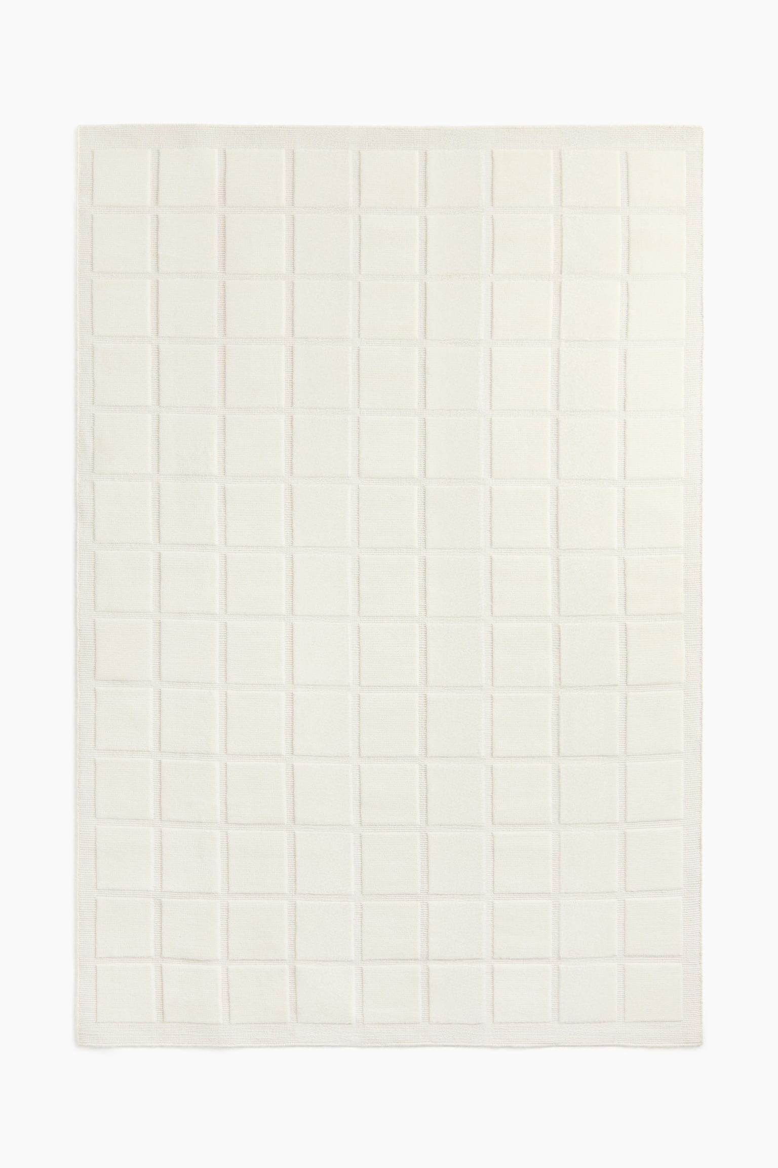 A cream-coloured blanket is lying flat, displaying a grid of raised square patterns across its surface and a subtle ribbed border. - 1