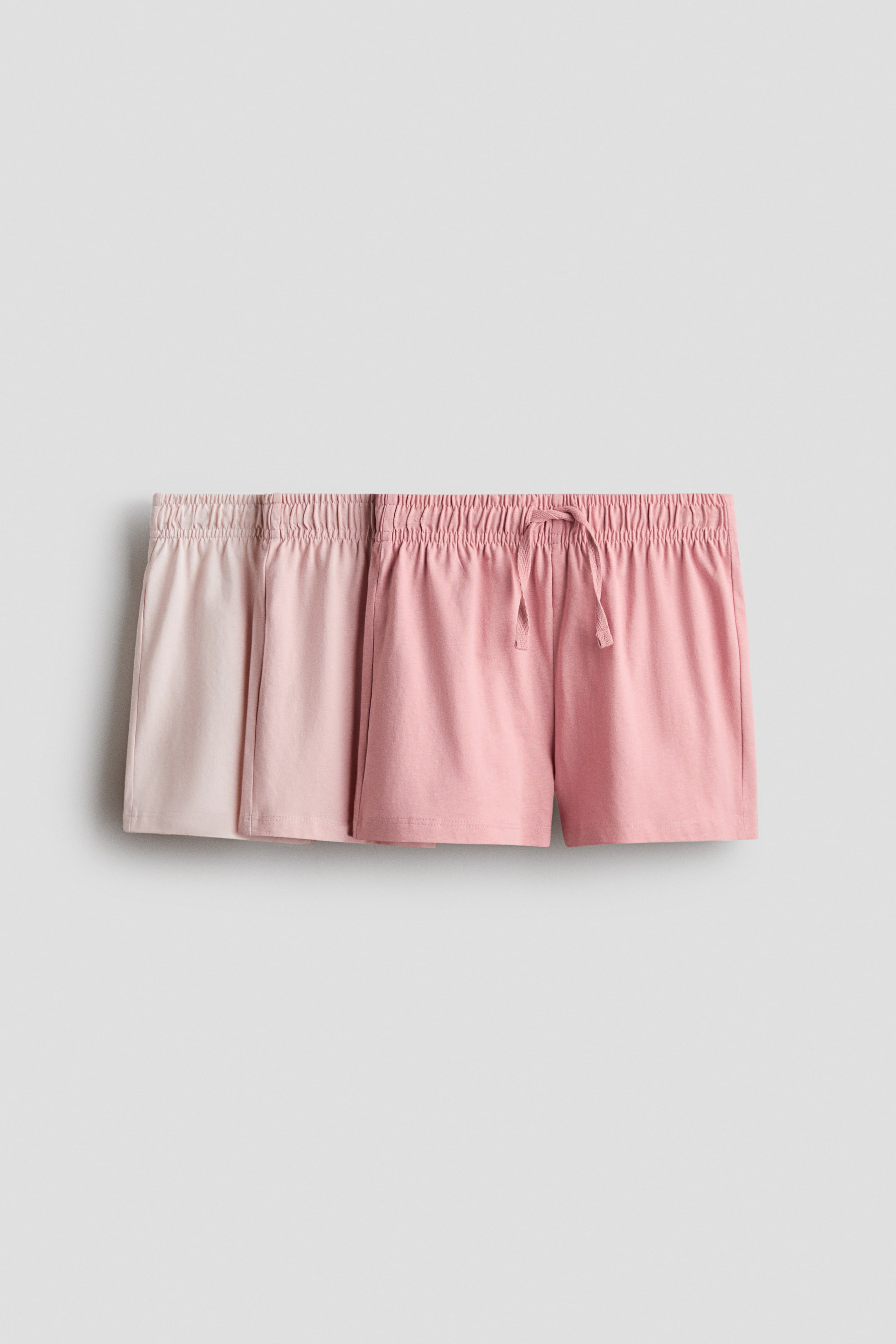 Visualizza immagine più grande: Due paia di pantaloncini, uno beige chiaro e uno rosa, sono presentati frontalmente. Entrambi i pantaloncini presentano fasce elasticizzate in vita con arricciature visibili, e il paio rosa dispone anche di un laccio da stringere sul davanti.