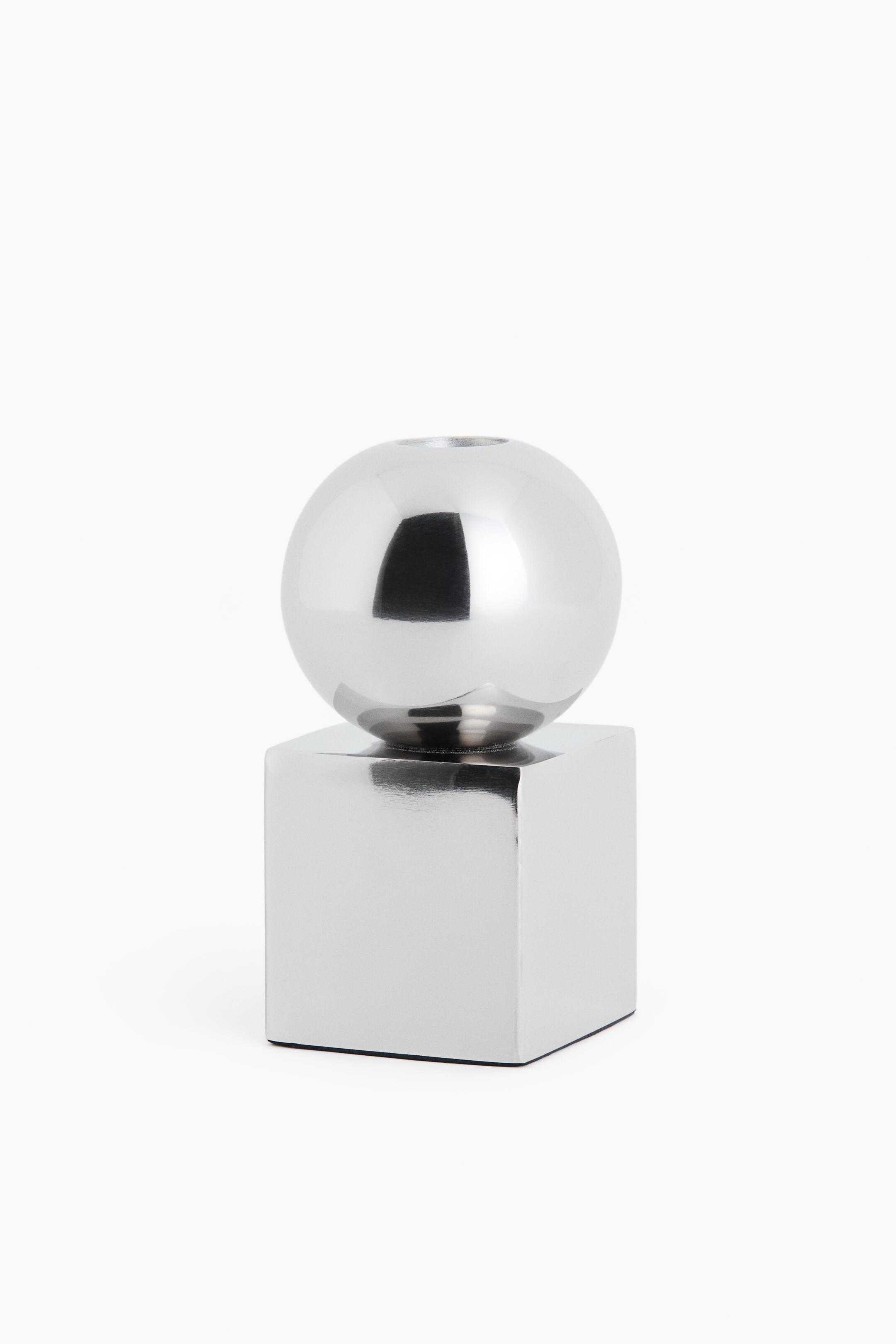 View larger image: A silver metallic candle holder is facing front, featuring a highly polished cube base that supports a matching spherical top. The sphere displays a small circular opening at its top centre, with both geometric sections reflecting light on their chrome-like surfaces.