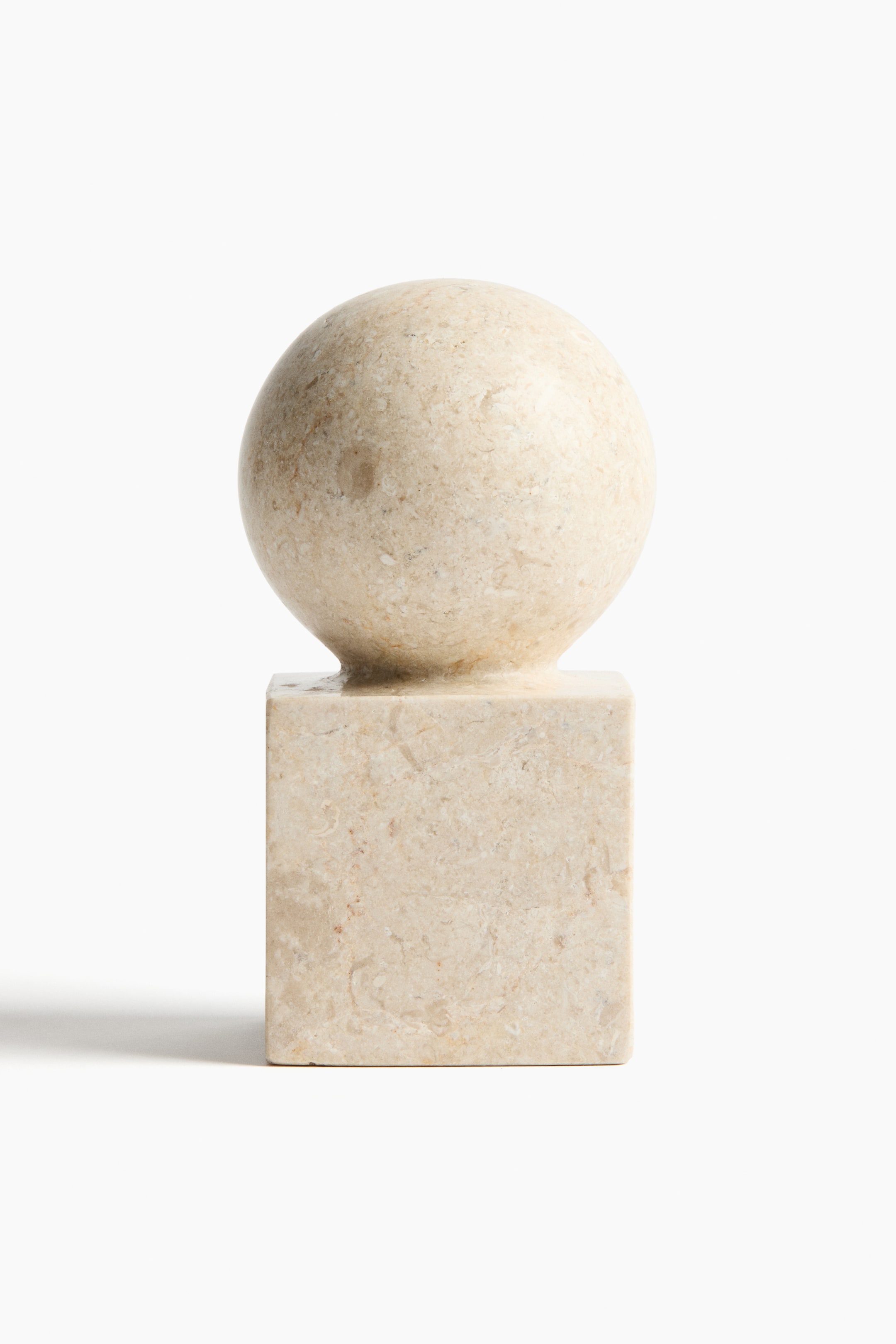 Grotere afbeelding bekijken: Een lichtbeige marmeren decoratief object wordt van voren getoond, met een bolvormige bovenkant die op een kubusvormige basis rust, waarbij beide delen subtiele natuurlijke aderpatronen vertonen.