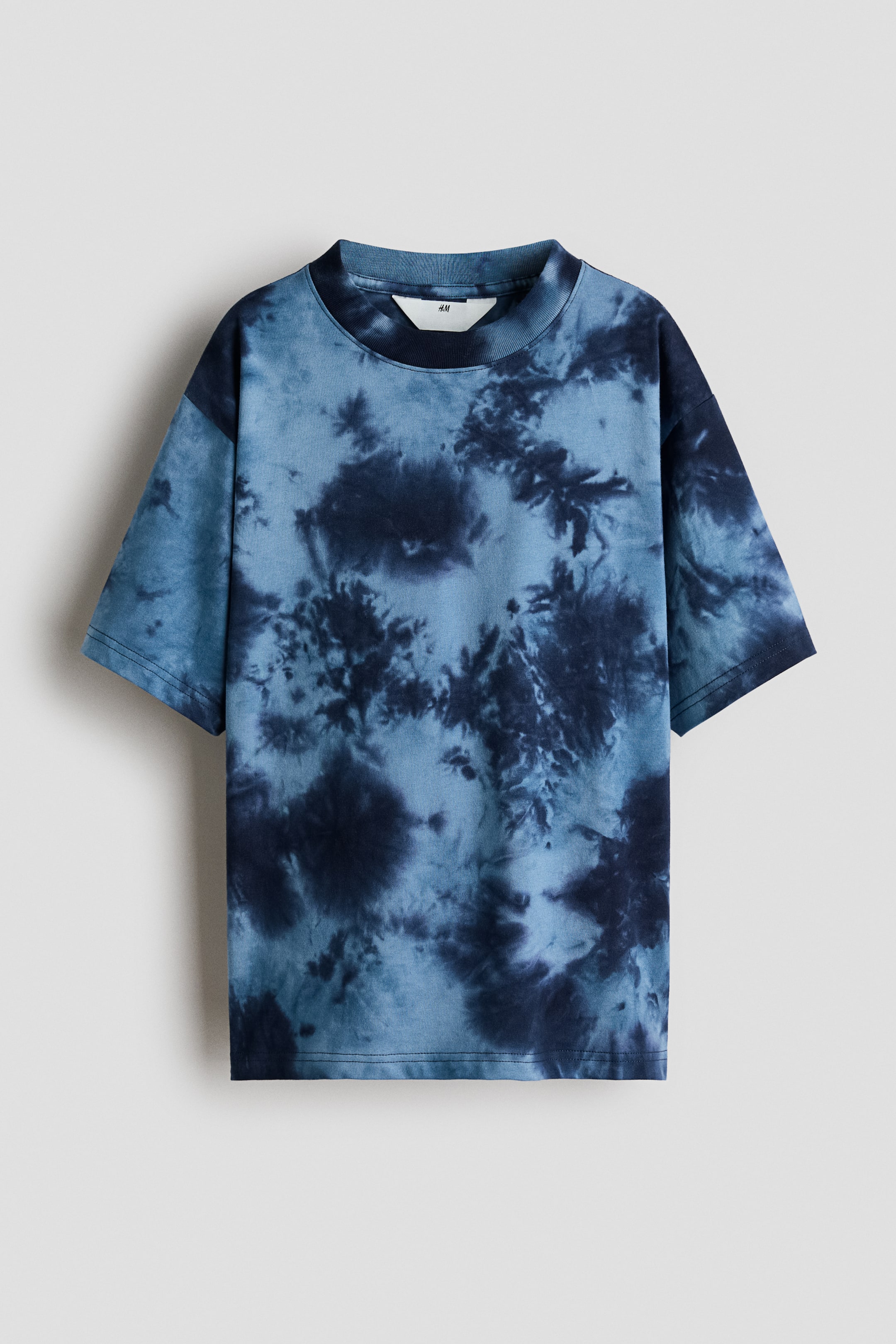 View larger image: A blue tie-dye T-shirt features a front-facing design with a mottled pattern in various shades of blue. It has a ribbed crew neck, short sleeves, and a white H&M label is visible on the inside back of the neck.
