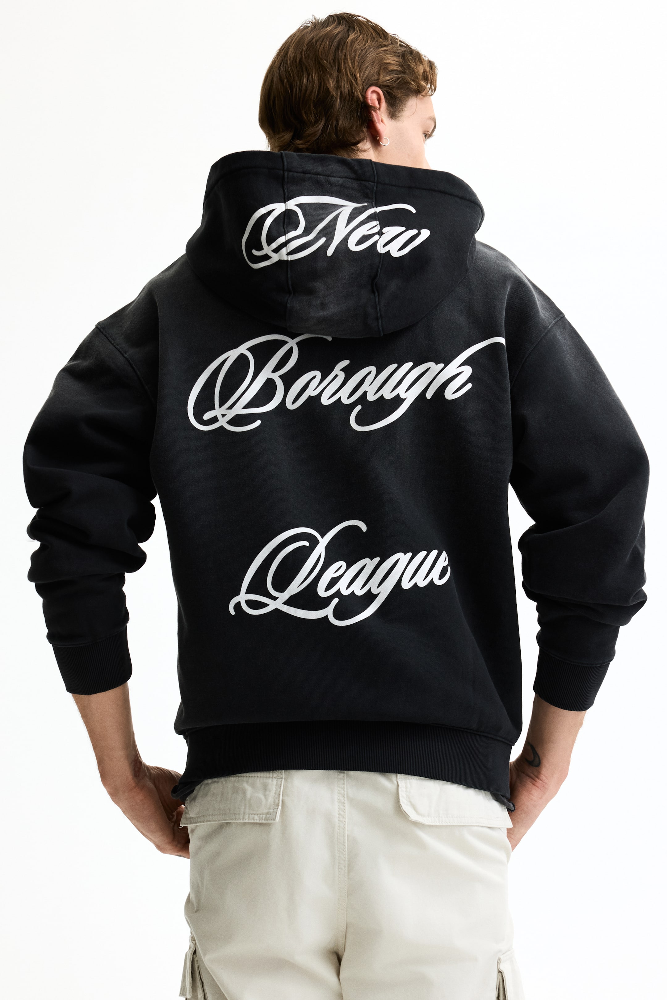 View larger image: A black hoodie is being showcased from the back, with "New Borough League" in white script across three lines on the garment's back. It features a hood, long sleeves with ribbed cuffs, and a ribbed hem.
