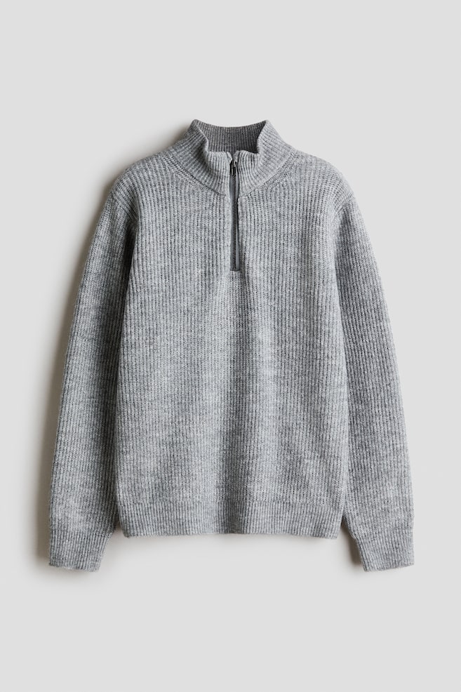 Ein grauer Pullover in Vorderansicht aus weichem Rippstrick mit hohem Kragen und halblangem ReiÃverschluss am Ausschnitt. Der Pullover zeigt sanft Ã¼berschnittene Schultern, lange Ãrmel mit RippbÃ¼ndchen und einen gerippten Saum. - 1