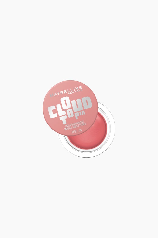 En Maybelline Cloud Topia Cheek & Lip Mousse fremviser en rund beholder, set ovenfra i en let skrå vinkel. Dets lyserøde låg, med teksten "Maybelline New York Cloud Topia Cheek & Lip Mousse" i sølvbogstaver, står delvist åbent og afslører en lys lyserød mousse i den gennemsigtige bund. - 1