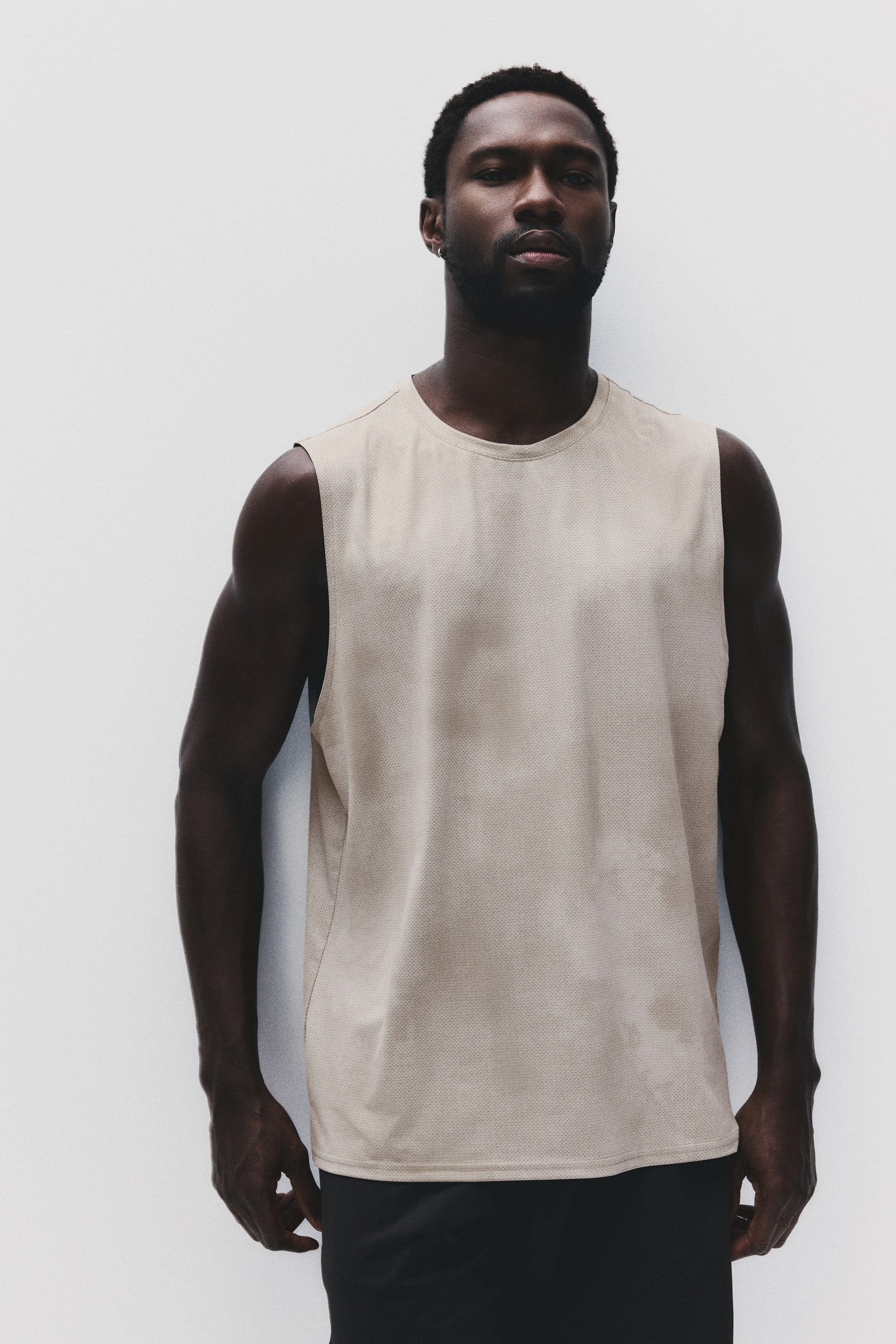 View larger image: A beige sleeveless top featuring a round neckline, a subtly textured knit fabric, and a straight hem, showcased facing forward.