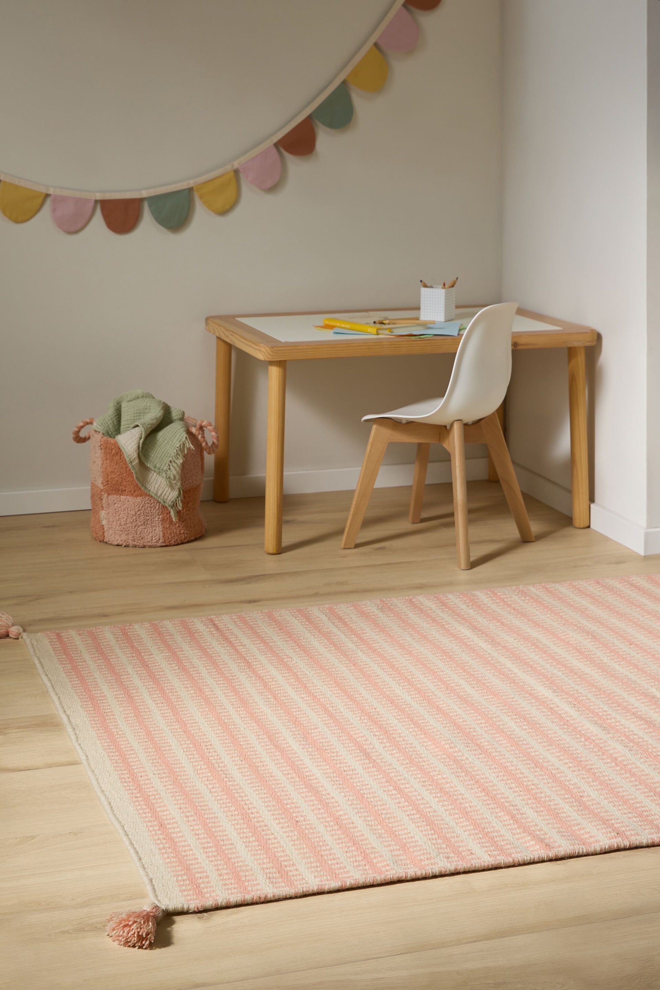 Ver imagen más grande: Una alfombra rectangular tejida se encuentra extendida, con un patrón de rayas alternas en tonos rosa y crema. Las rayas crema presentan una textura de chevron sutil, y borlas rosas son visibles en las esquinas.