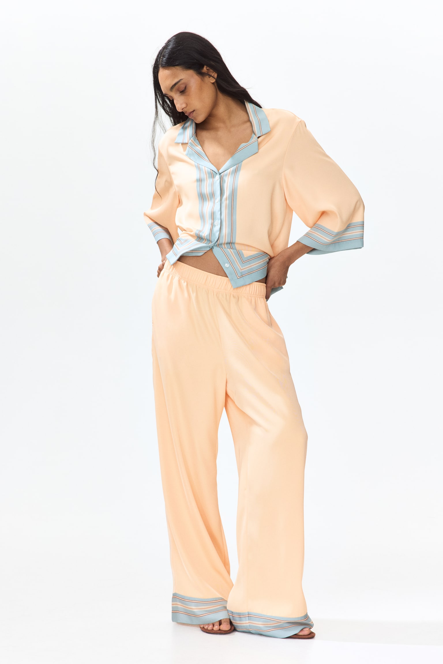 The peach-coloured wide-leg trousers showcase an elasticated waistband. The trouser hems feature a light blue band accented with thin horizontal stripes in peach, brown, and light blue. - 1