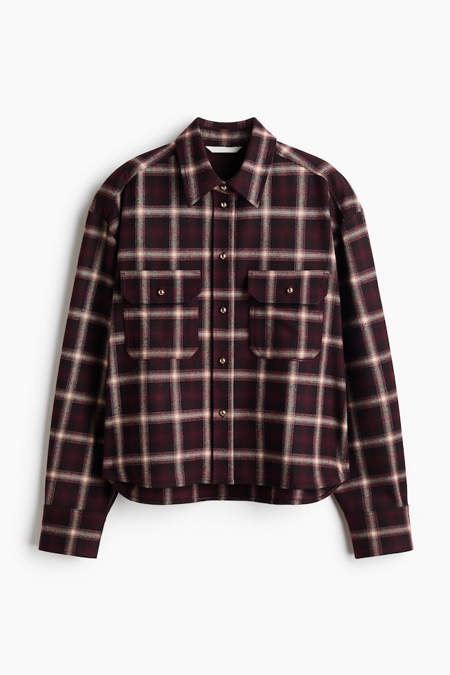 A front-facing, long-sleeved shirt is featuring a dark burgundy, cream, and grey plaid pattern. It is showcasing a point collar, a central button-down closure with gold-toned metallic buttons, dropped shoulders, and two chest flap pockets with button closures. - 1