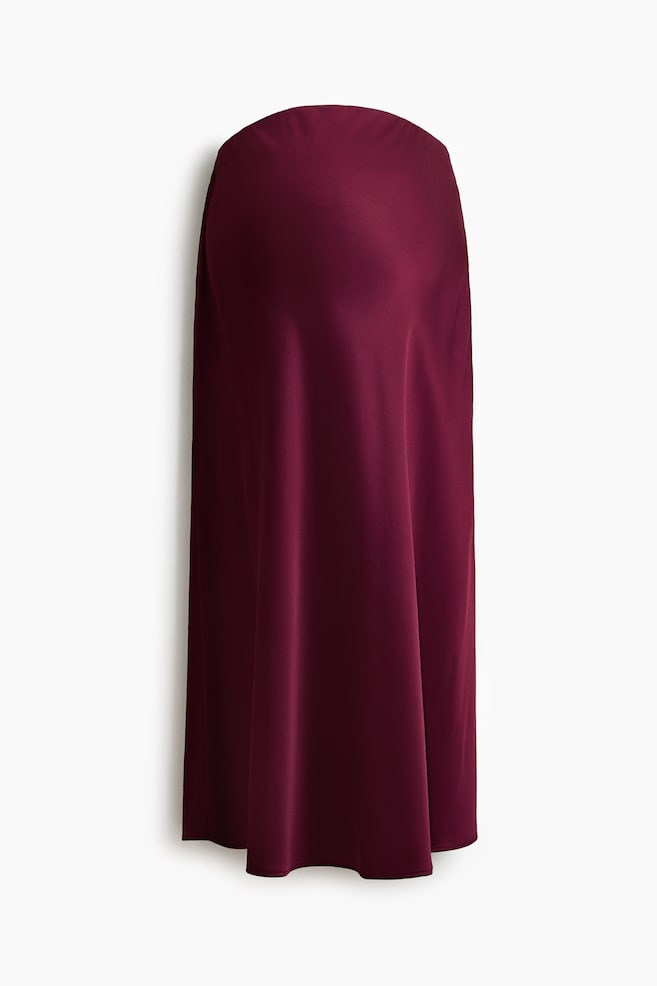 A calf-length satin skirt in deep burgundy is shown front-facing, featuring a high-waisted silhouette with softly draping fabric. The material falls in gentle, fluid folds toward a straight hemline, highlighting its smooth texture and subtle sheen. - 1