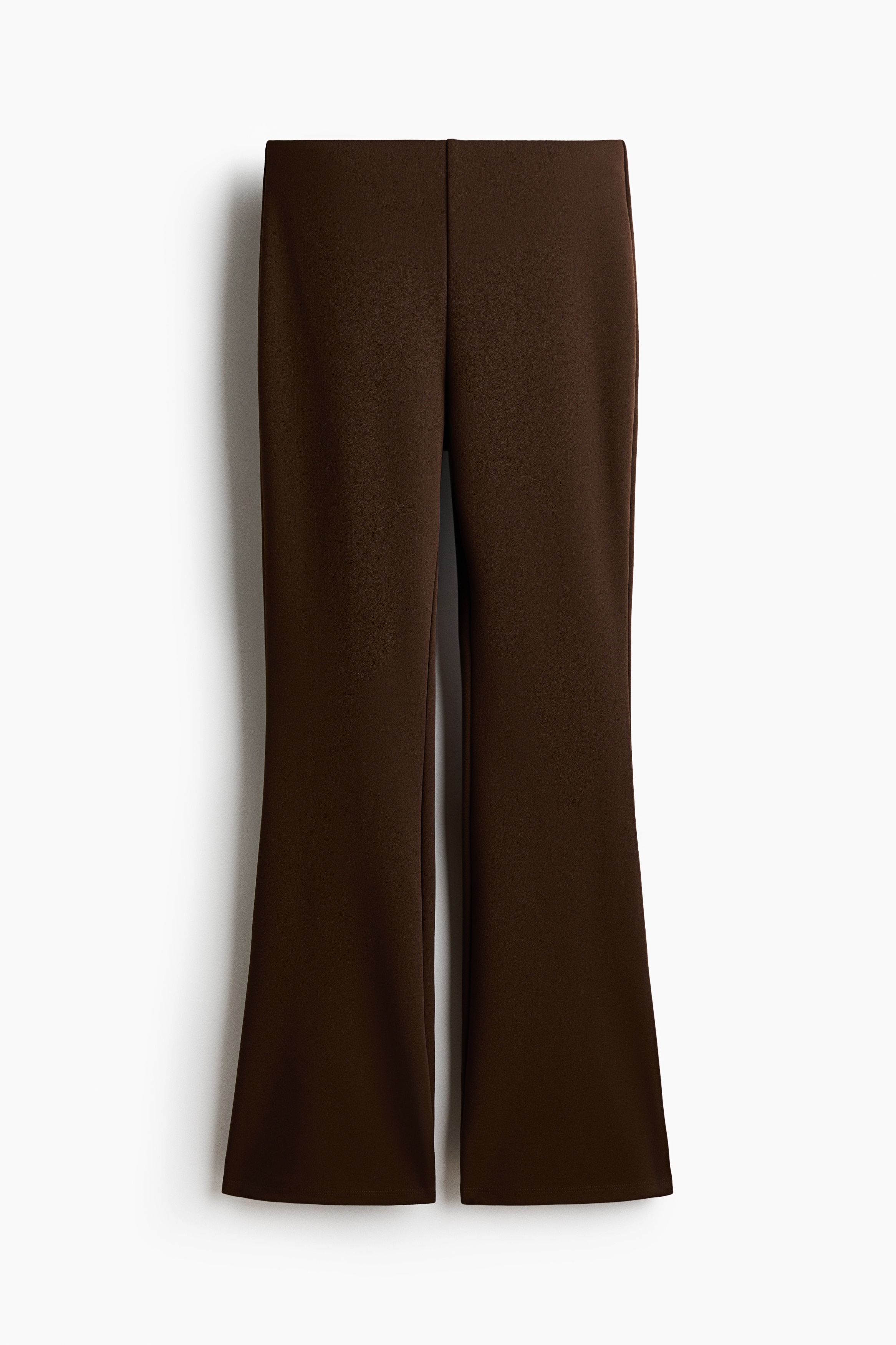 The model is wearing brown flared leggings, featuring a fitted silhouette through the thigh that widens into a flare at the hem. The leggings are styled as a matching set with a sleeveless brown vest cinched at the waist with a thin belt.