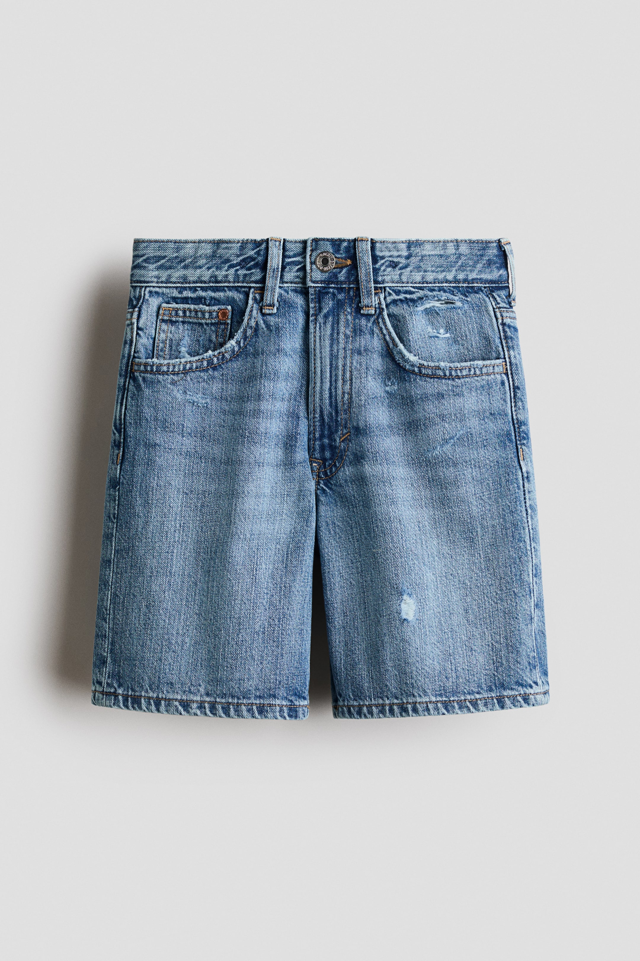 View larger image: Front-facing 5-pocket light blue denim shorts showcase a faded wash with distressed details and slight abrasions. They offer a loose fit through the hip and thigh, complete with belt loops, and feature a zip fly with a button closure at the waistband.