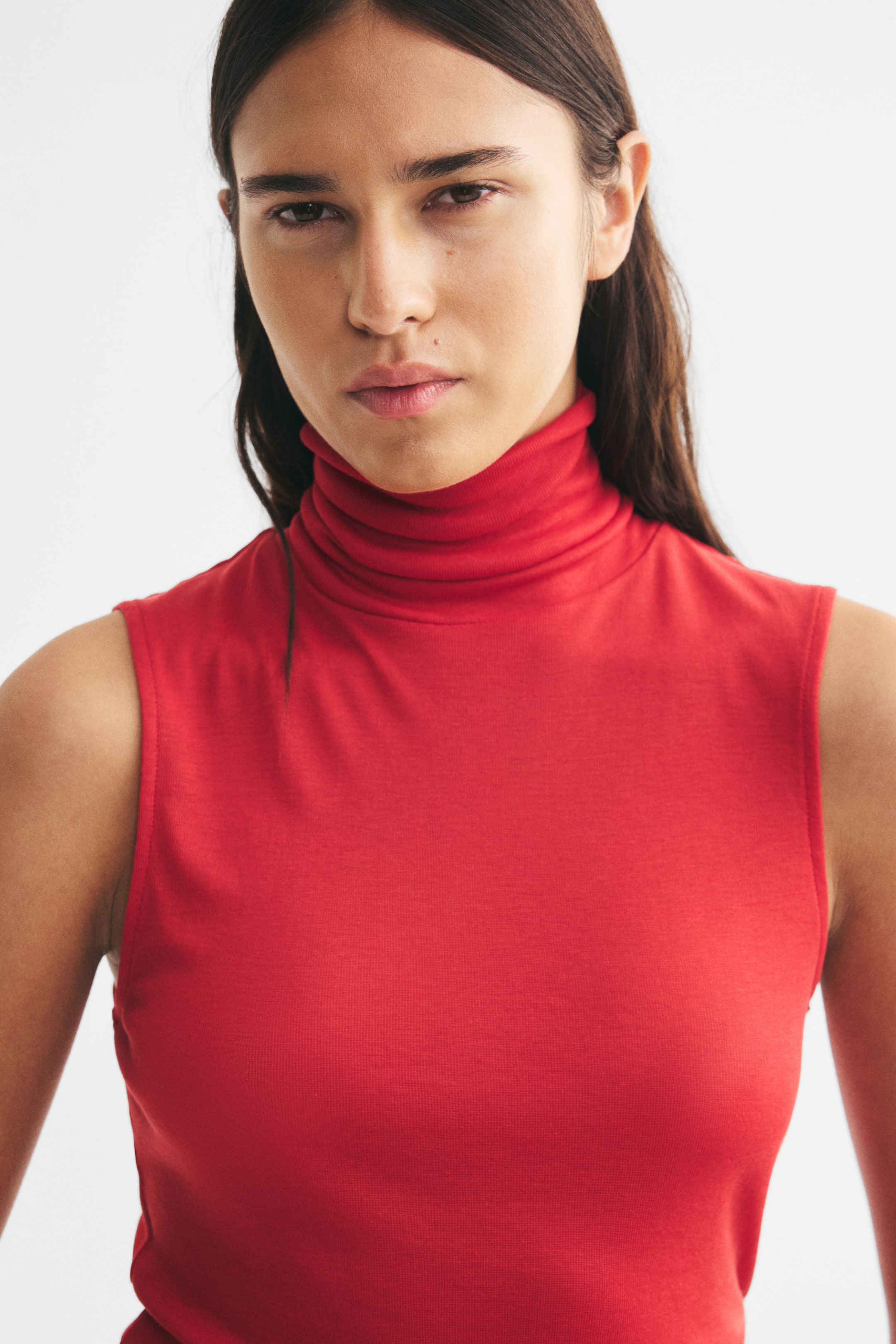 View larger image: The model is wearing a red, sleeveless fine-knit top featuring a high turtleneck.