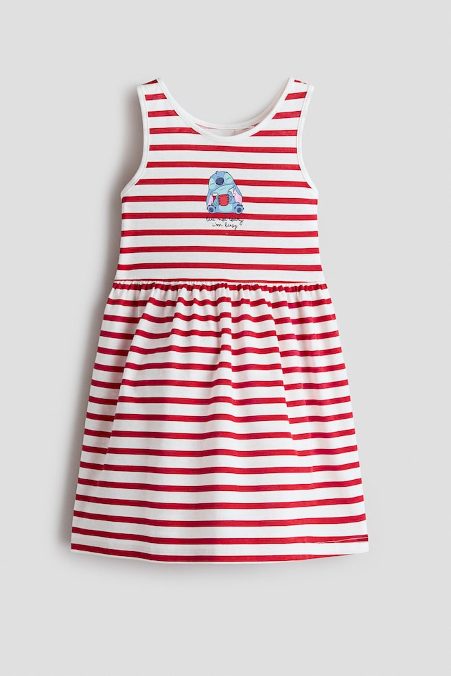 A sleeveless cotton jersey dress is shown from the front, featuring an all-over pattern of red and white horizontal stripes. The dress is displaying a round neckline, a gathered seam at the waist that creates a flared skirt, and a small cartoon graphic on the center chest. - 1