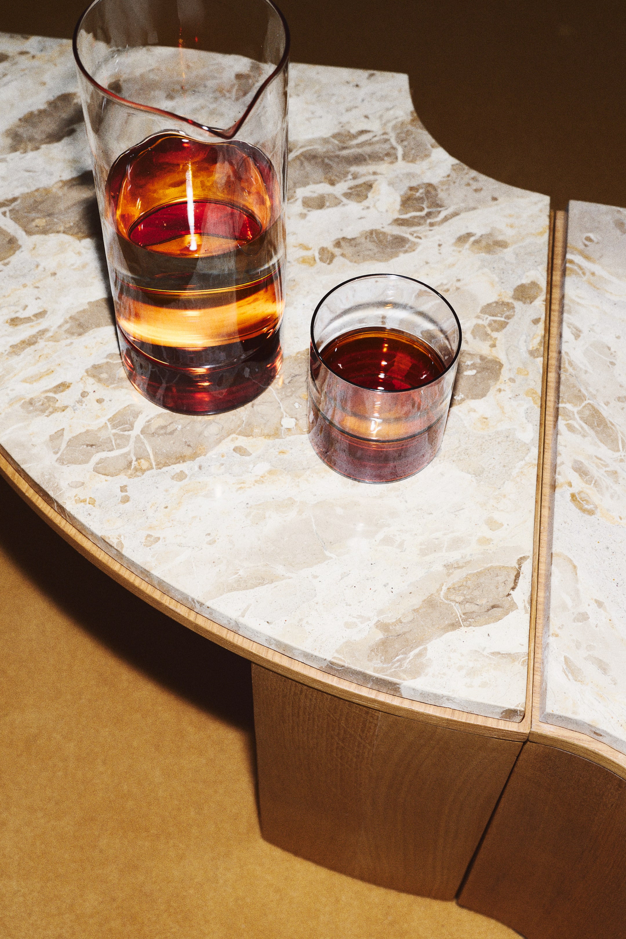 View larger image: A borosilicate glass tumbler is standing next to a matching tall glass pitcher, both featuring a clear upper section fused to a dark amber-coloured base.