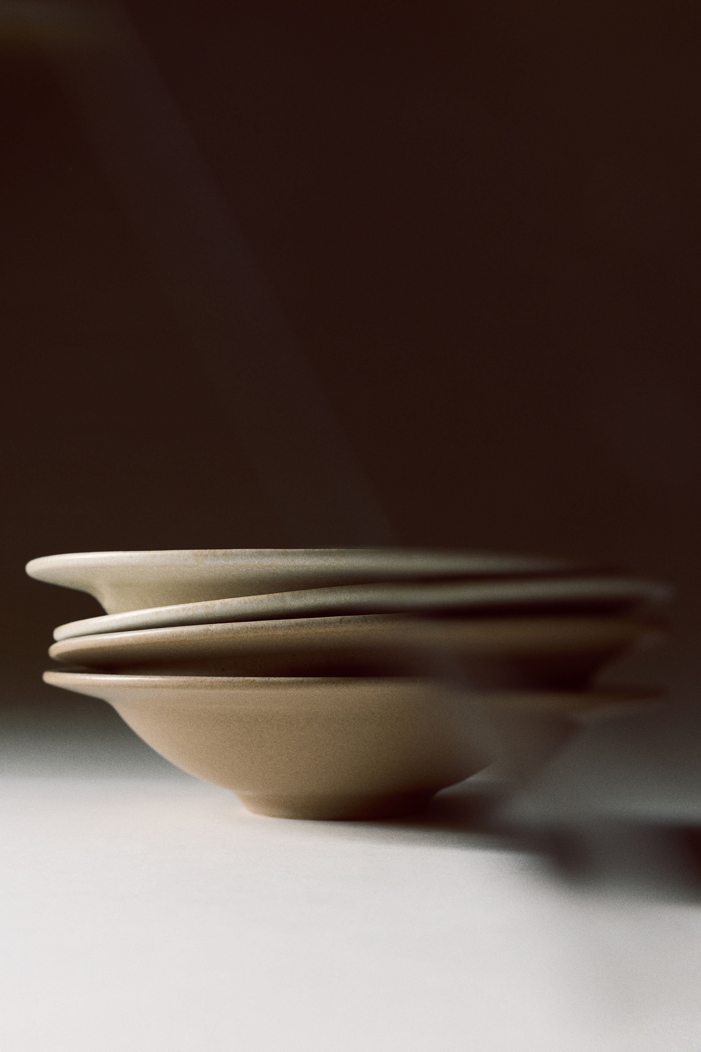Deux bols en cÃ©ramique beige apparaissent vus de dessus, alignÃ©s verticalement. Les deux bols prÃ©sentent un large rebord plat et un creux central profond, avec une glaÃ§ure mate texturÃ©e et mouchetÃ©e.