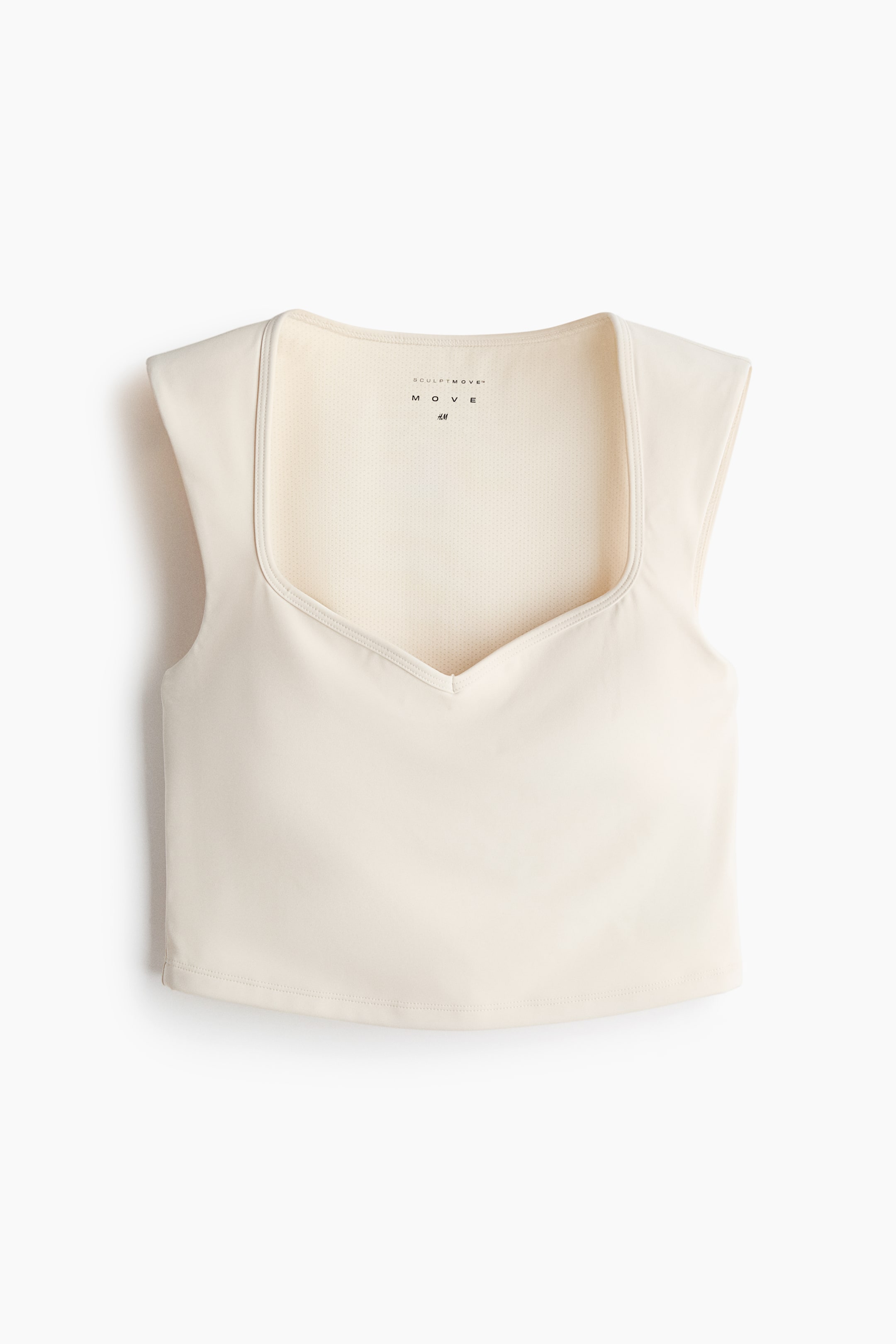 View larger image: A cream athletic crop top is shown from the front, featuring a square neckline with a sweetheart dip and wide cap sleeves. The neckline's visible interior lining shows a textured mesh fabric.
