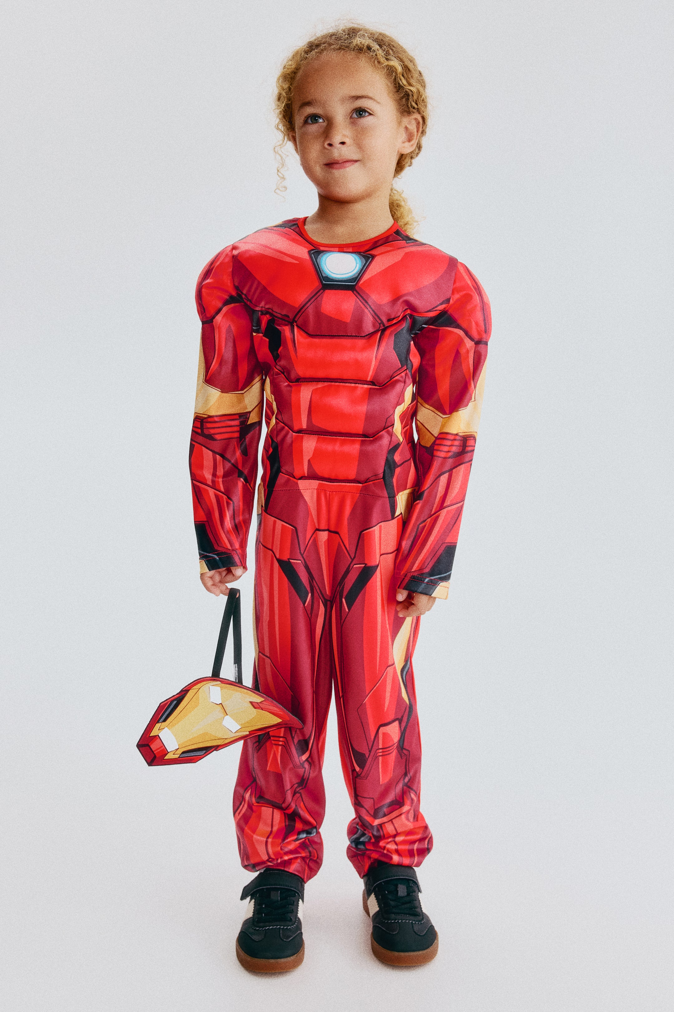 View larger image: A fancy dress costume features a red and gold full-body jumpsuit with padded sections on the chest, shoulders, arms and legs, creating an armoured appearance, and the front of the jumpsuit includes a light blue and white circular arc reactor detail on the chest. A matching red and yellow mask is held.