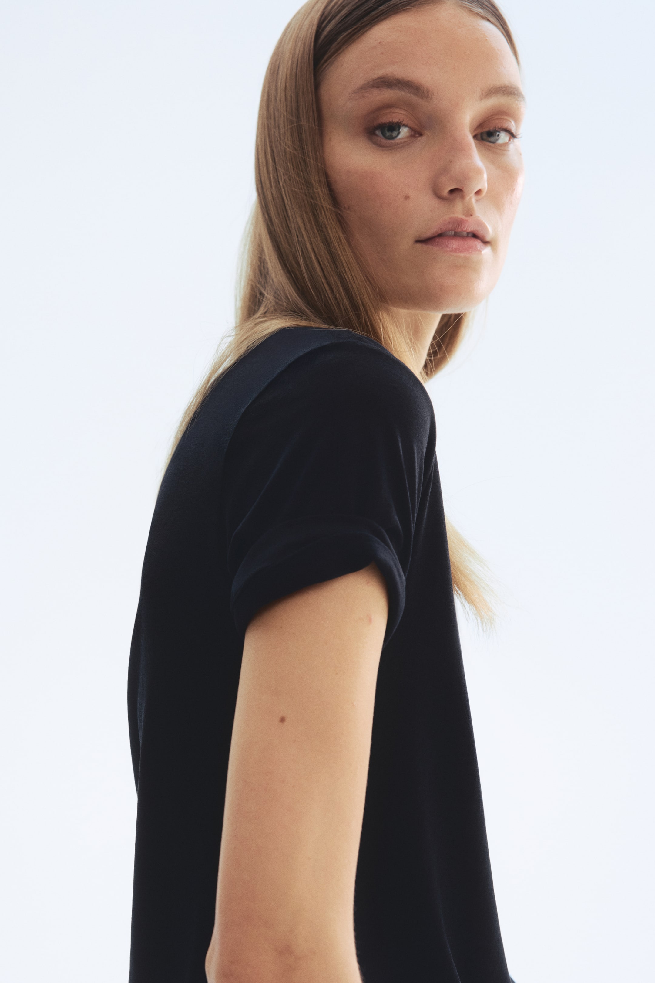 View larger image: A black t-shirt is viewed from a side angle, showcasing short sleeves that are cuffed. The fabric looks soft and drapes elegantly.