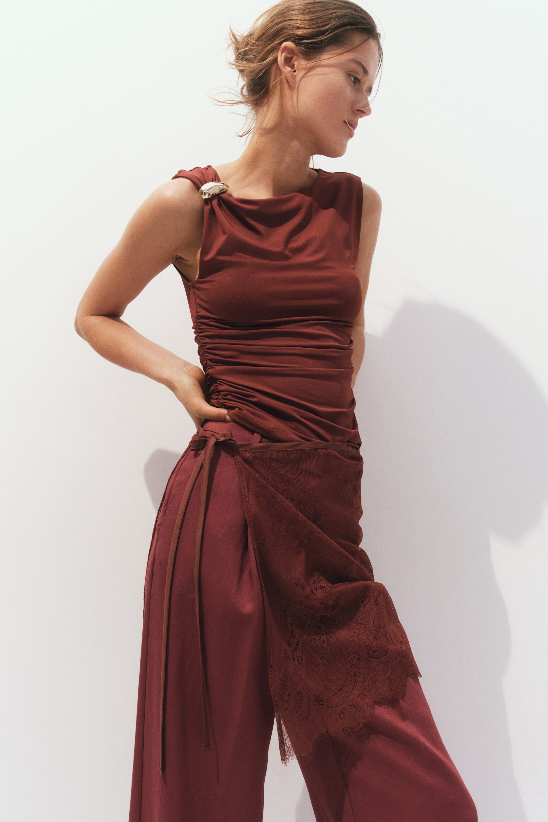 Voir une image plus grande: Un haut sans manches rouge foncé présente un décolleté drapé, des détails froncés sur le torse et une broche métallique ornée rassemblant le tissu sur une épaule. Un pantalon large assorti rouge foncé est doté d'une superposition latérale avec de fines attaches et d'un panneau en dentelle à bord festonné, présenté sous un angle de vue de face.