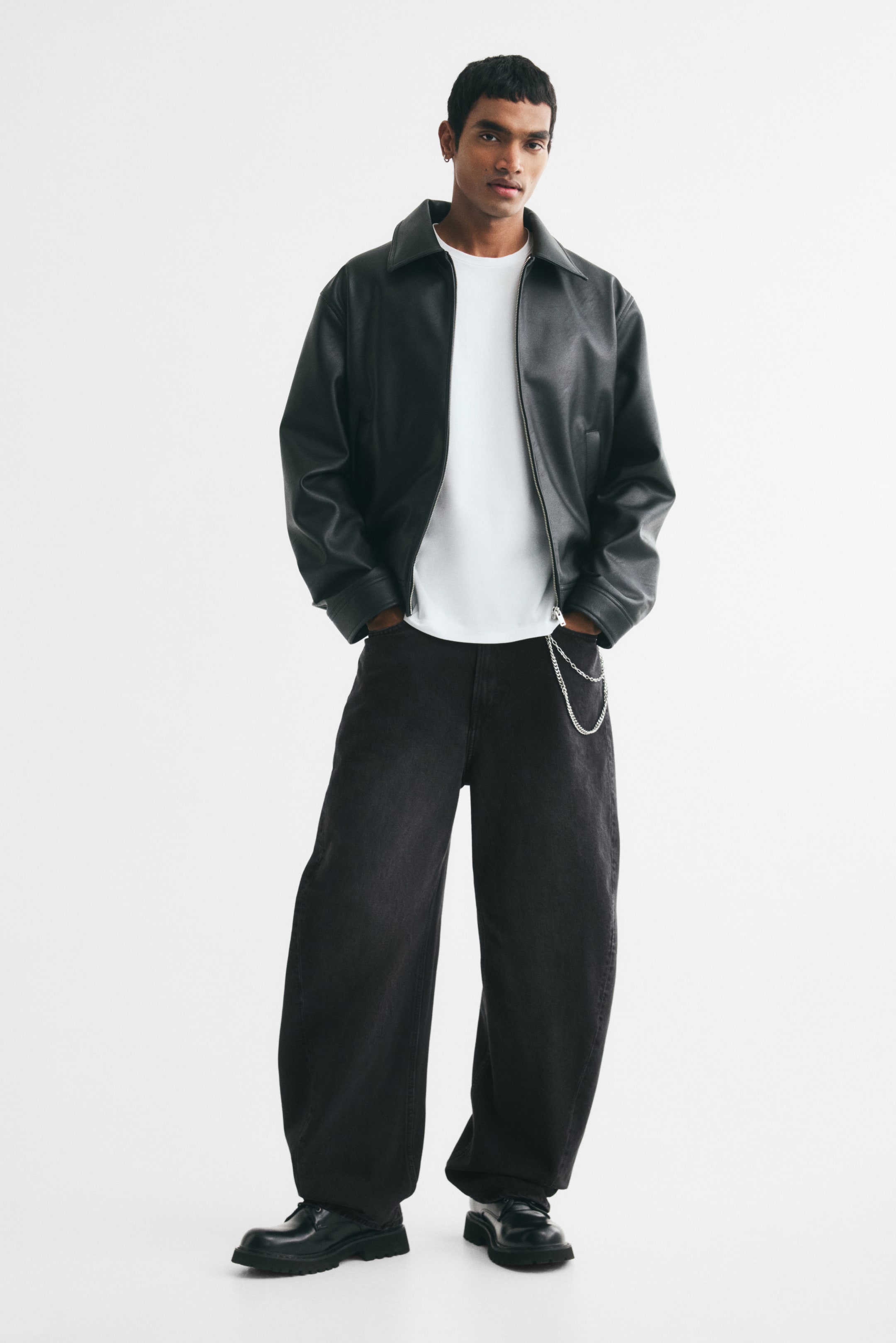 View larger image: The model is wearing a black bomber jacket with a wide collar and a center zipper closure, layered over a white crew-neck T-shirt.