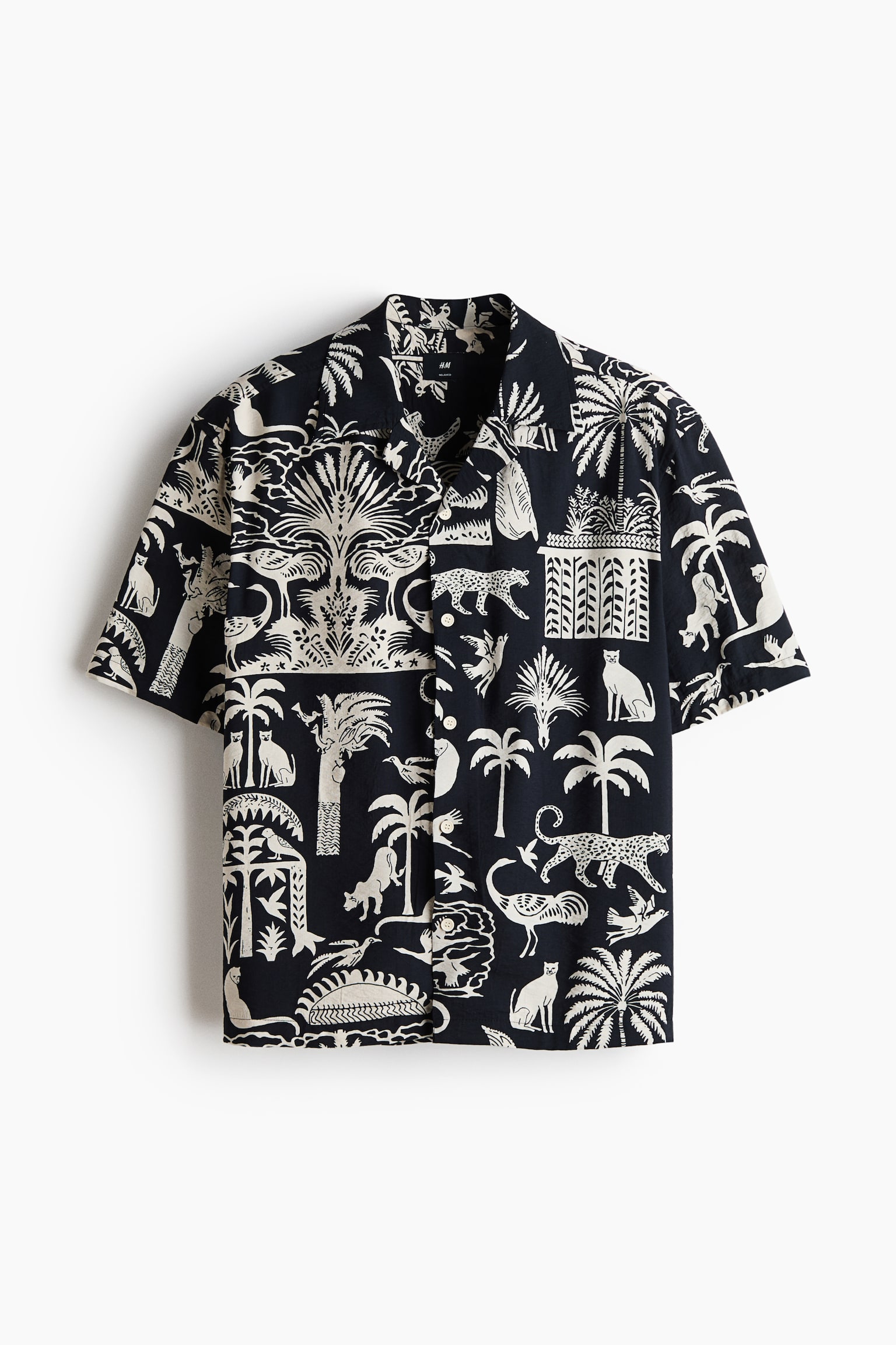 The short-sleeved shirt showcases a black and off-white tropical pattern across its front. It features a revere collar, a button-front fastening with visible white buttons, and short sleeves. The pattern depicts various animals, including leopards and cats, alongside palm trees and other foliage. - 1